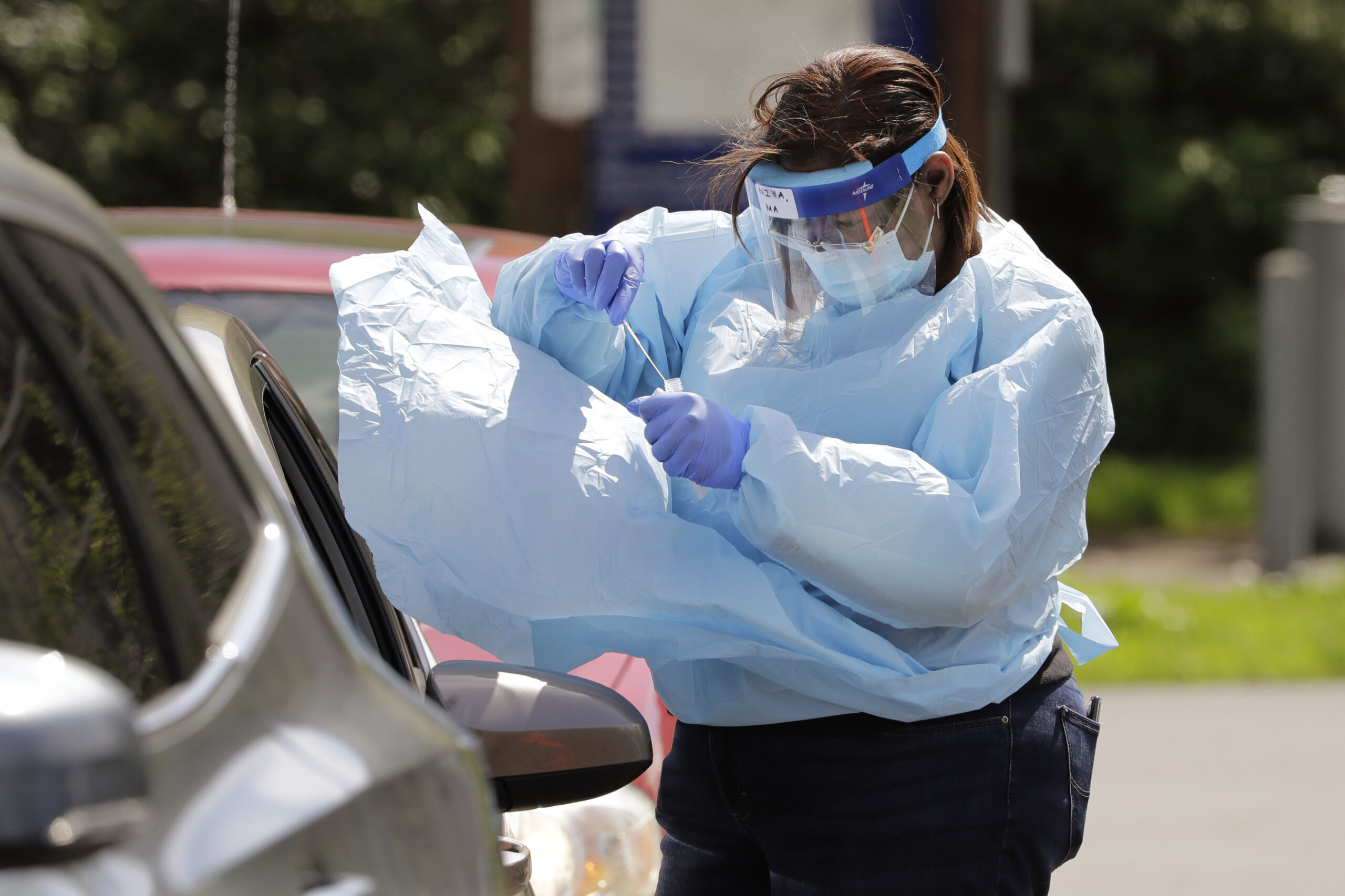 A medical assistant reaches in to take a nasal swab from a driver at a drive-up coronavirus testing site