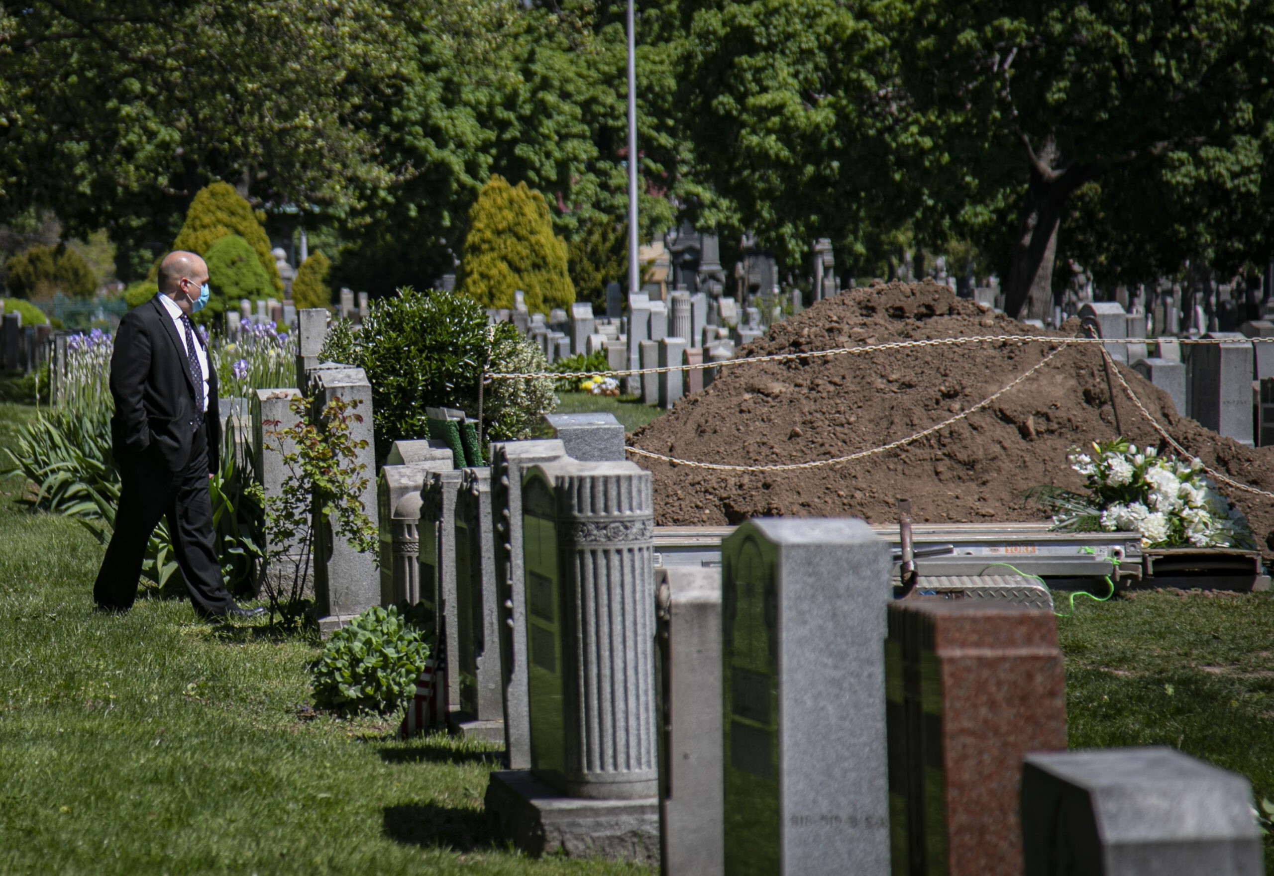 Robert Salerno, a funeral director, wears a mask as he reviews a gravesite
