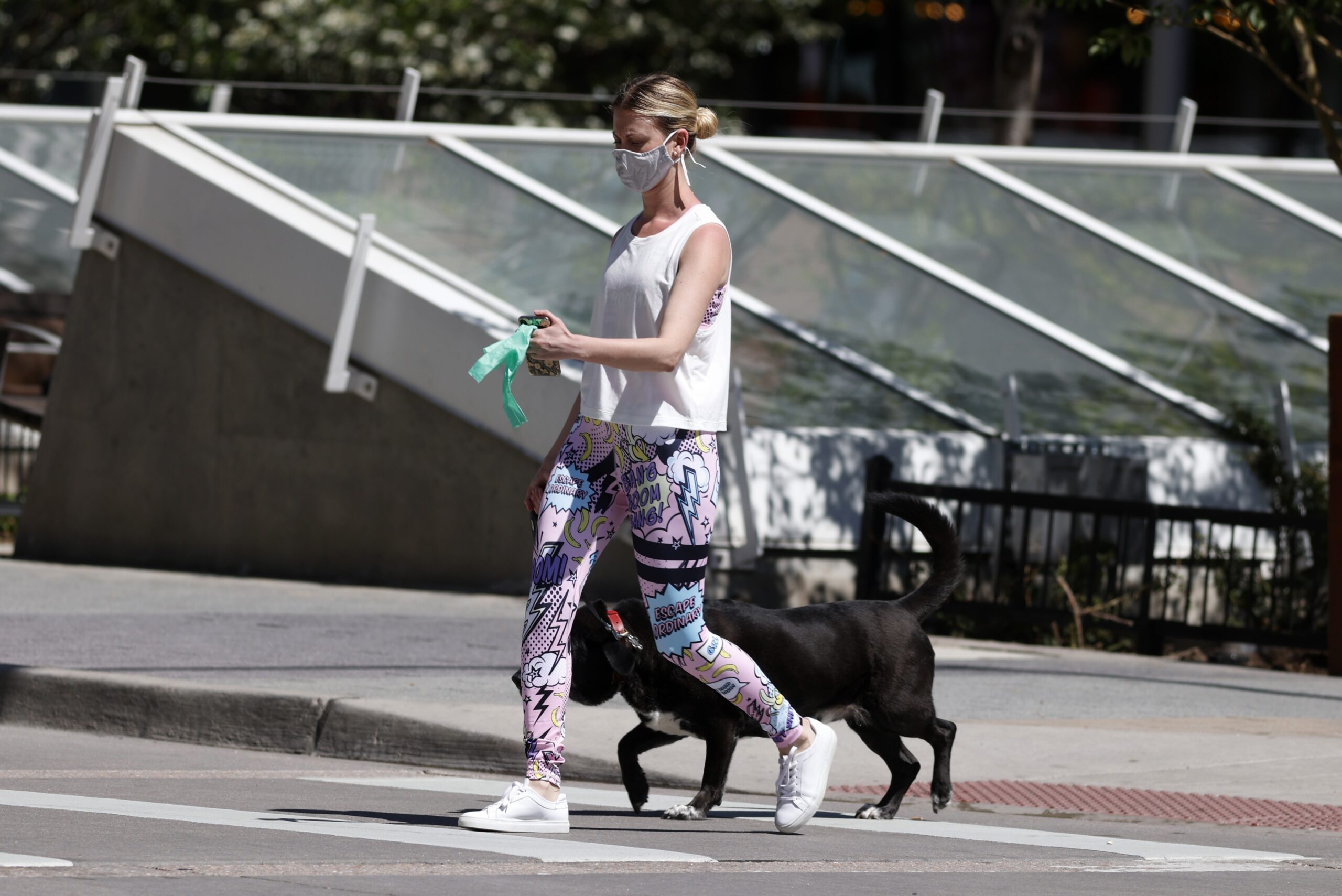 A pedestrian in a face mask leads her dog across across the street