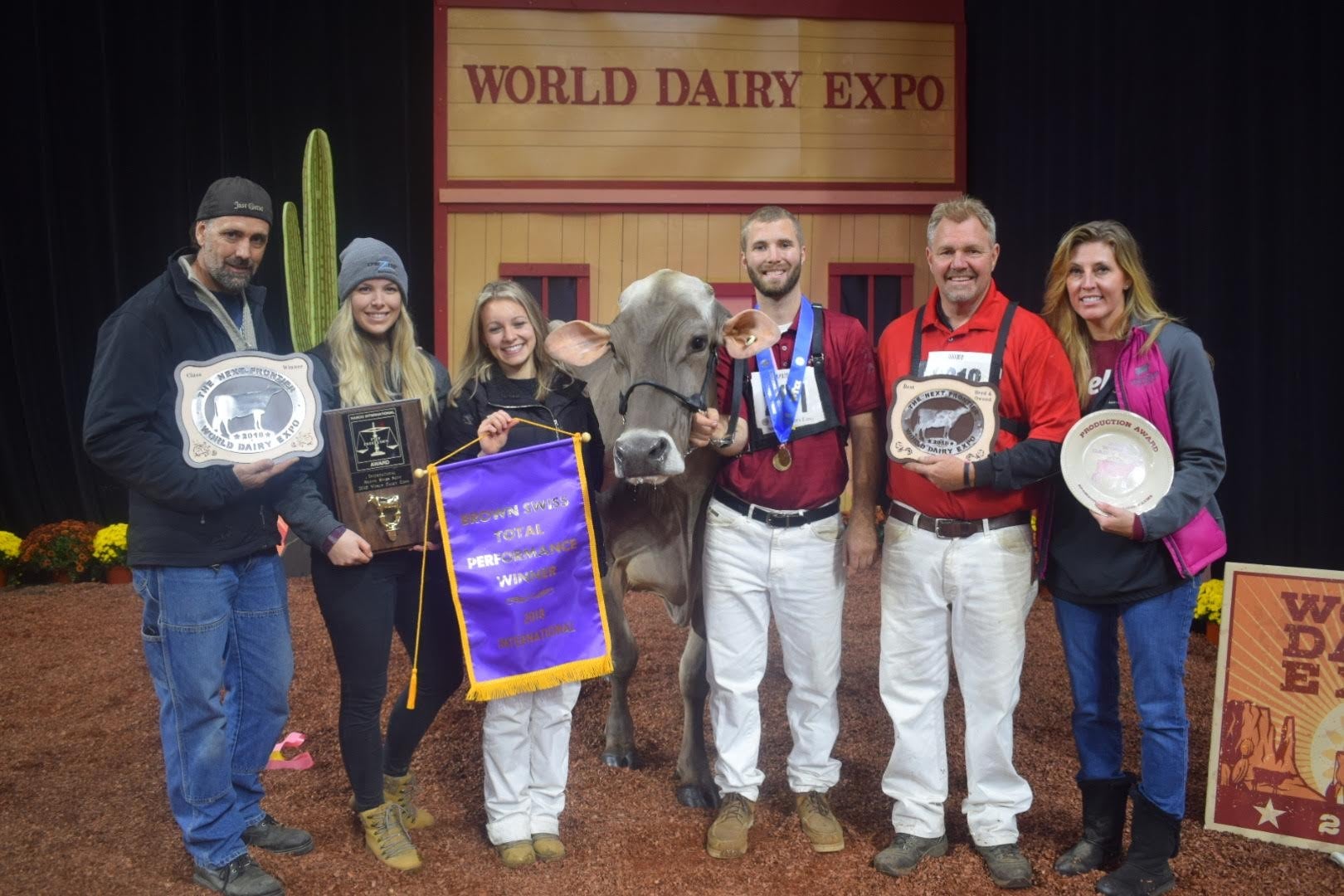 a dairy farmer poses with his family and a cow