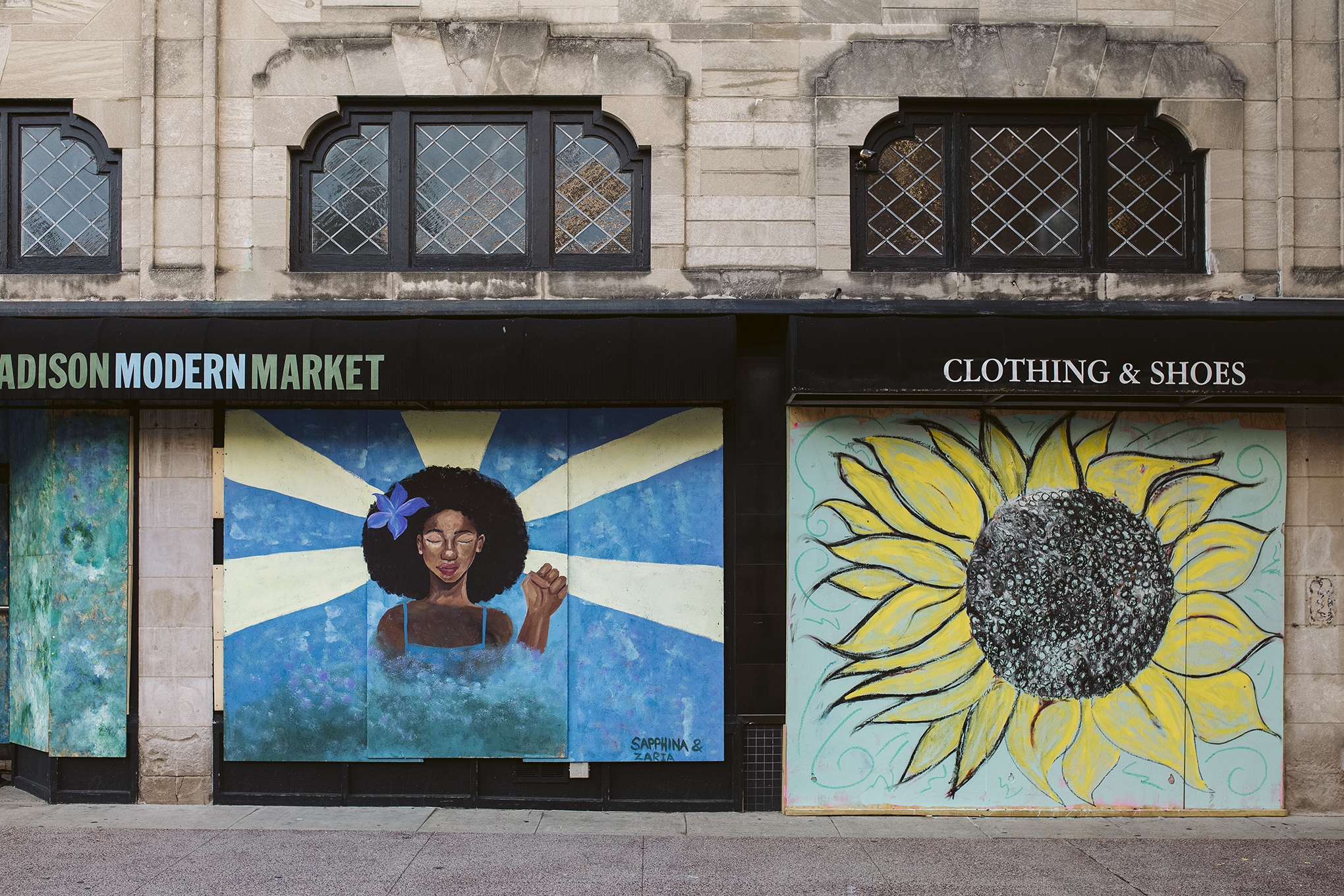 Artwork by Sapphina and Zaria is displayed on boarded up store windows on State Street