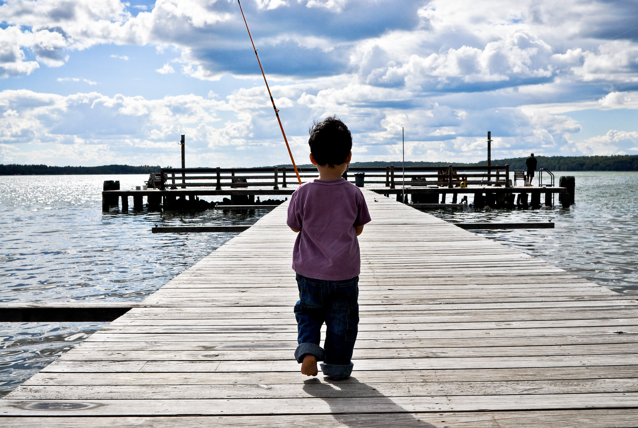 Small boy walking on dock with fishing pole.