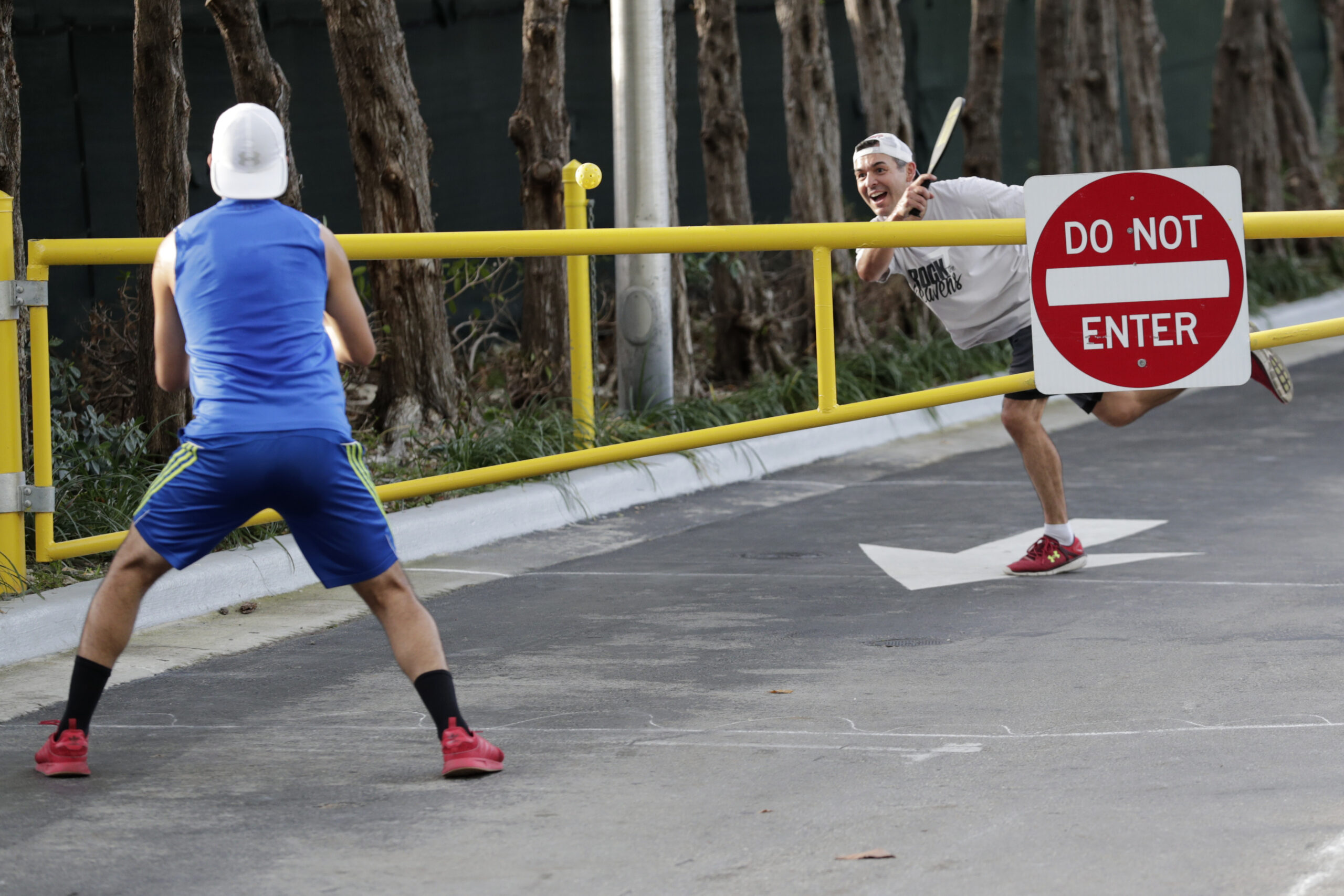 A father and son use a metal park gate as an improvised net for a pickleball game.