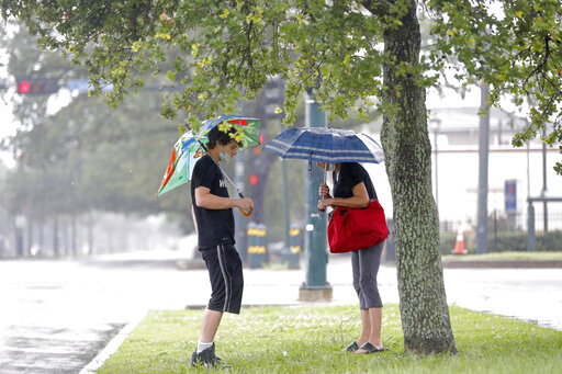 A mom and son stand under their umbrellas in a grassy area near the bus stop.