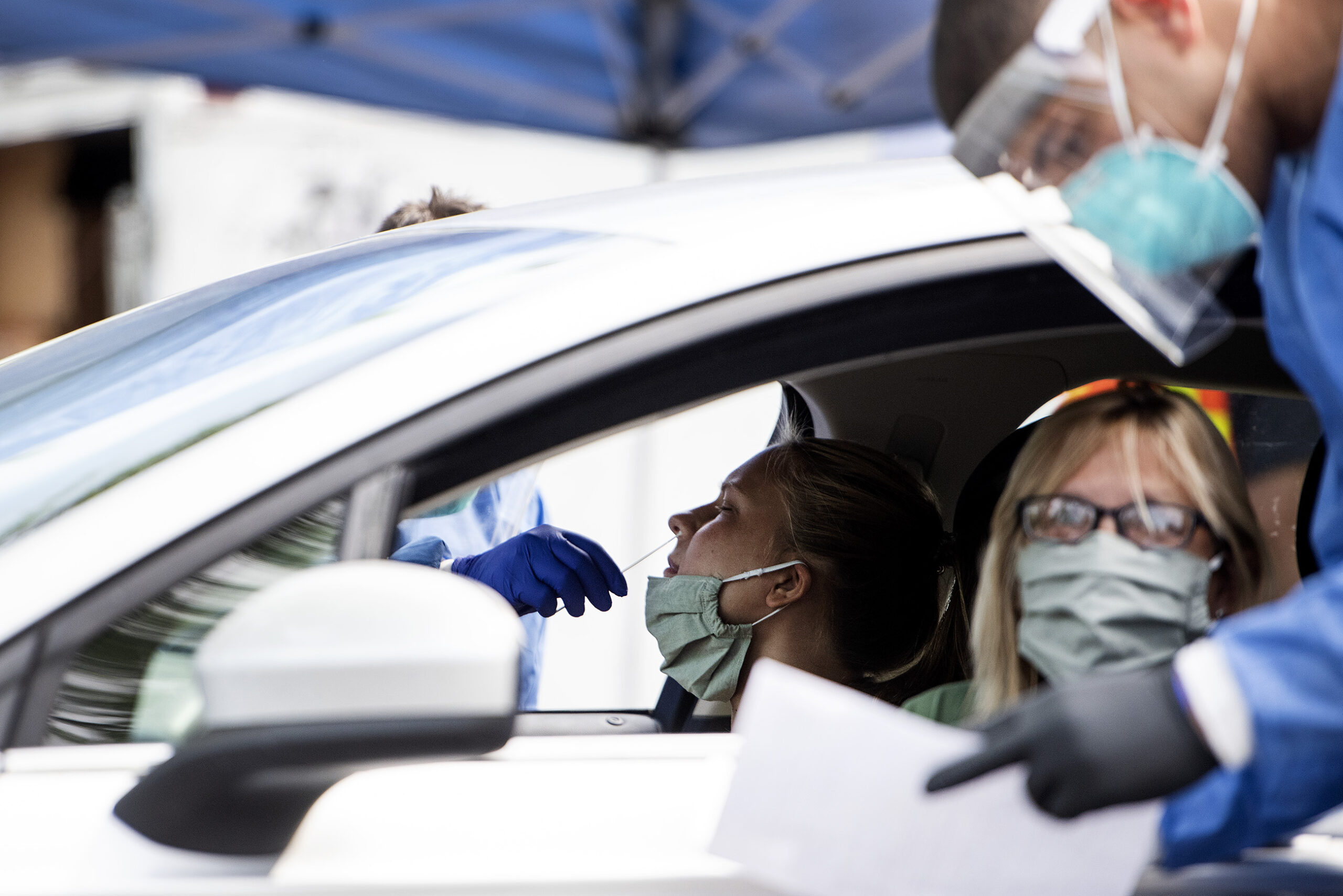 A woman leans back in a car as her nose is swabbed for COVID-19
