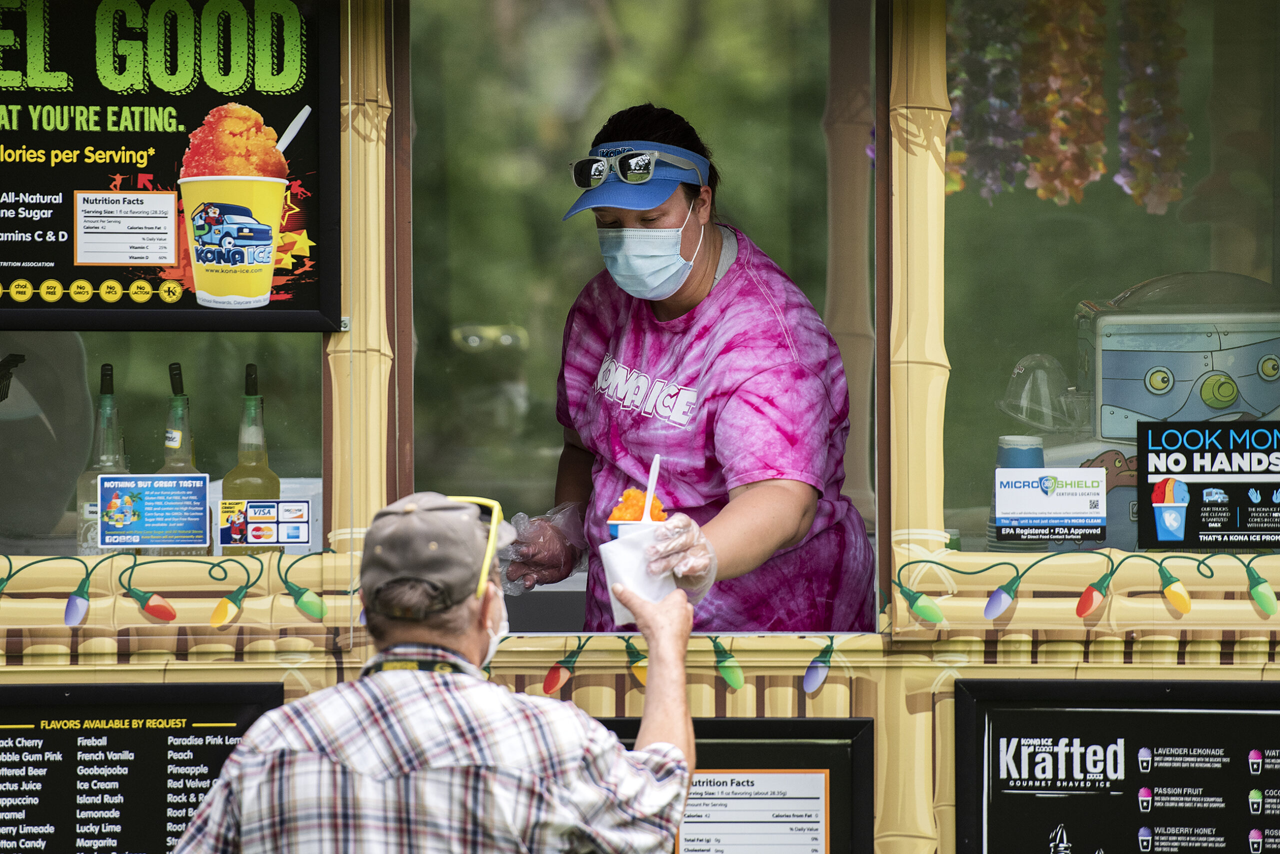 A woman in a mask hands a frozen treat to a customer from a food truck