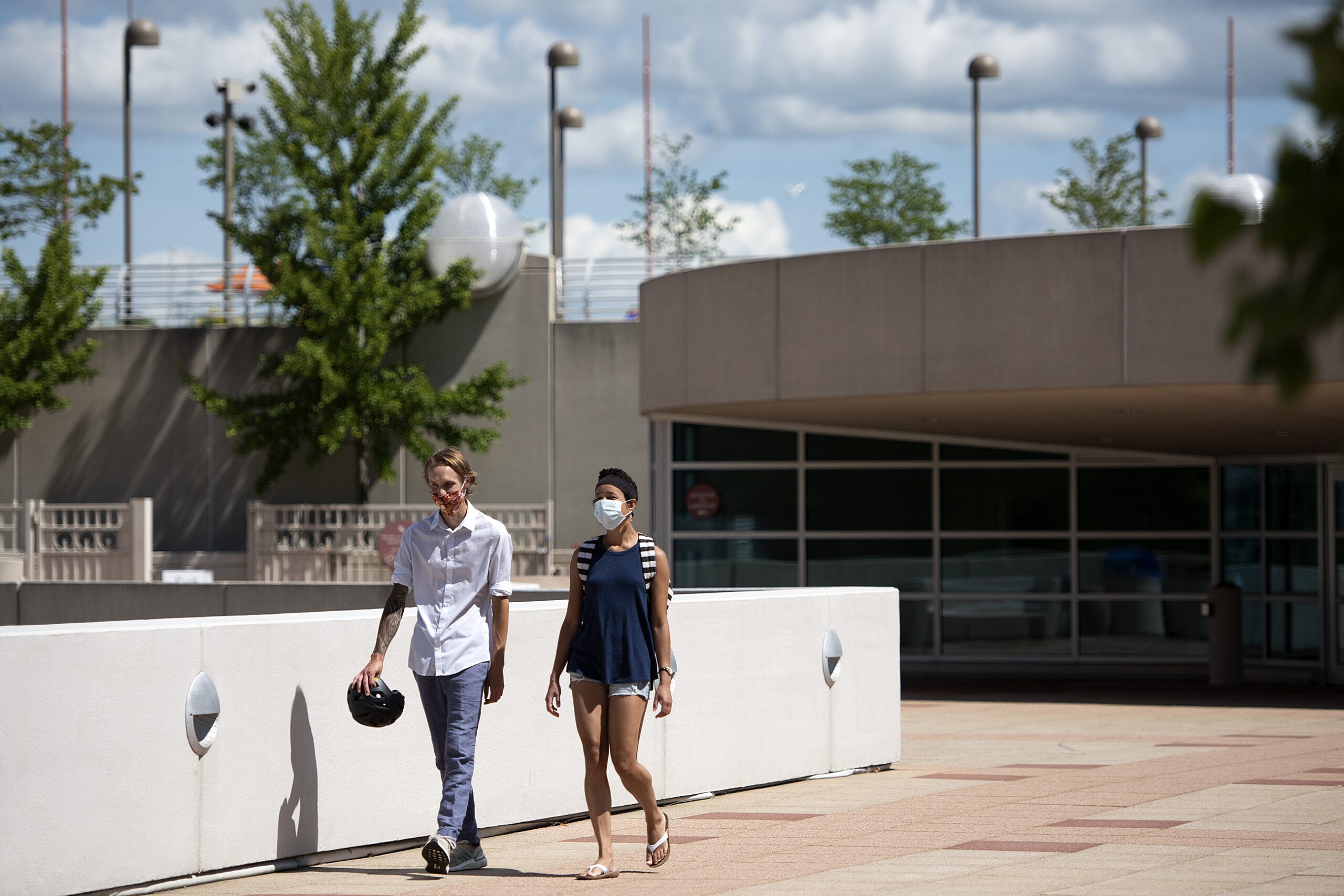 Two people walk on a sunny day while wearing masks