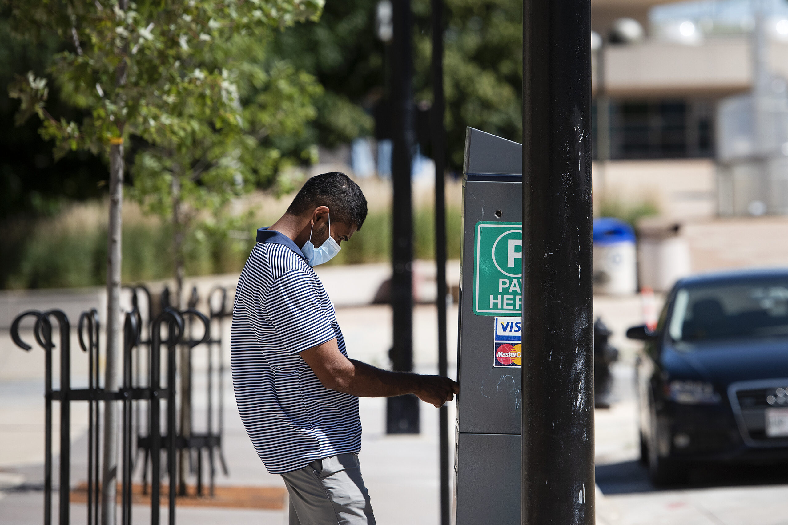 A man pays at a parking meter machine while wearing a mask