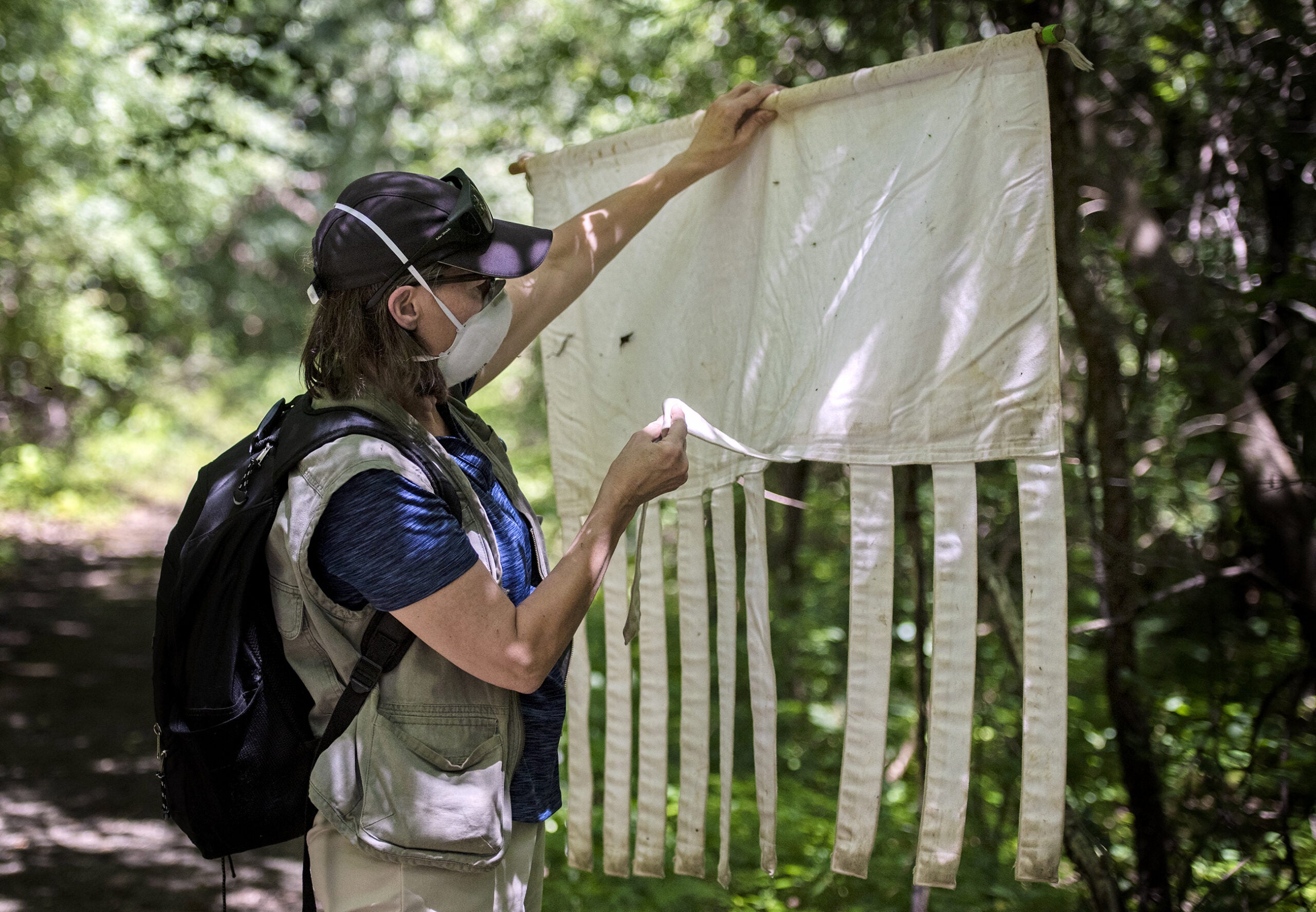 A woman examines a long piece of white canvas with strands at the end