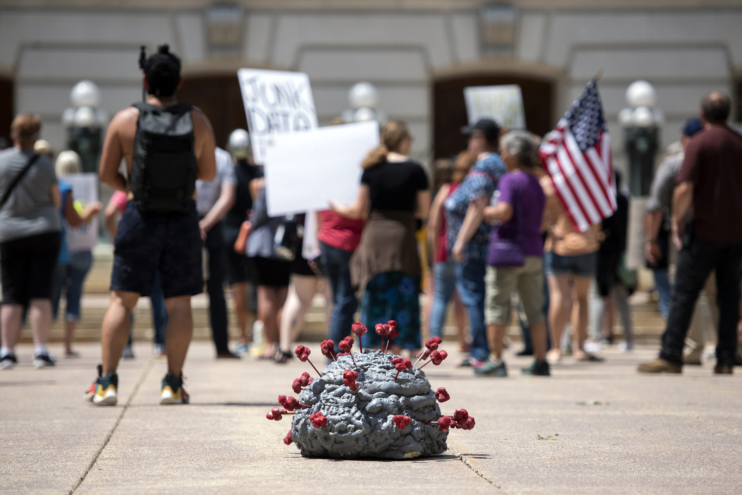 A model of the coronavirus is on the ground in front of anti-mask protesters