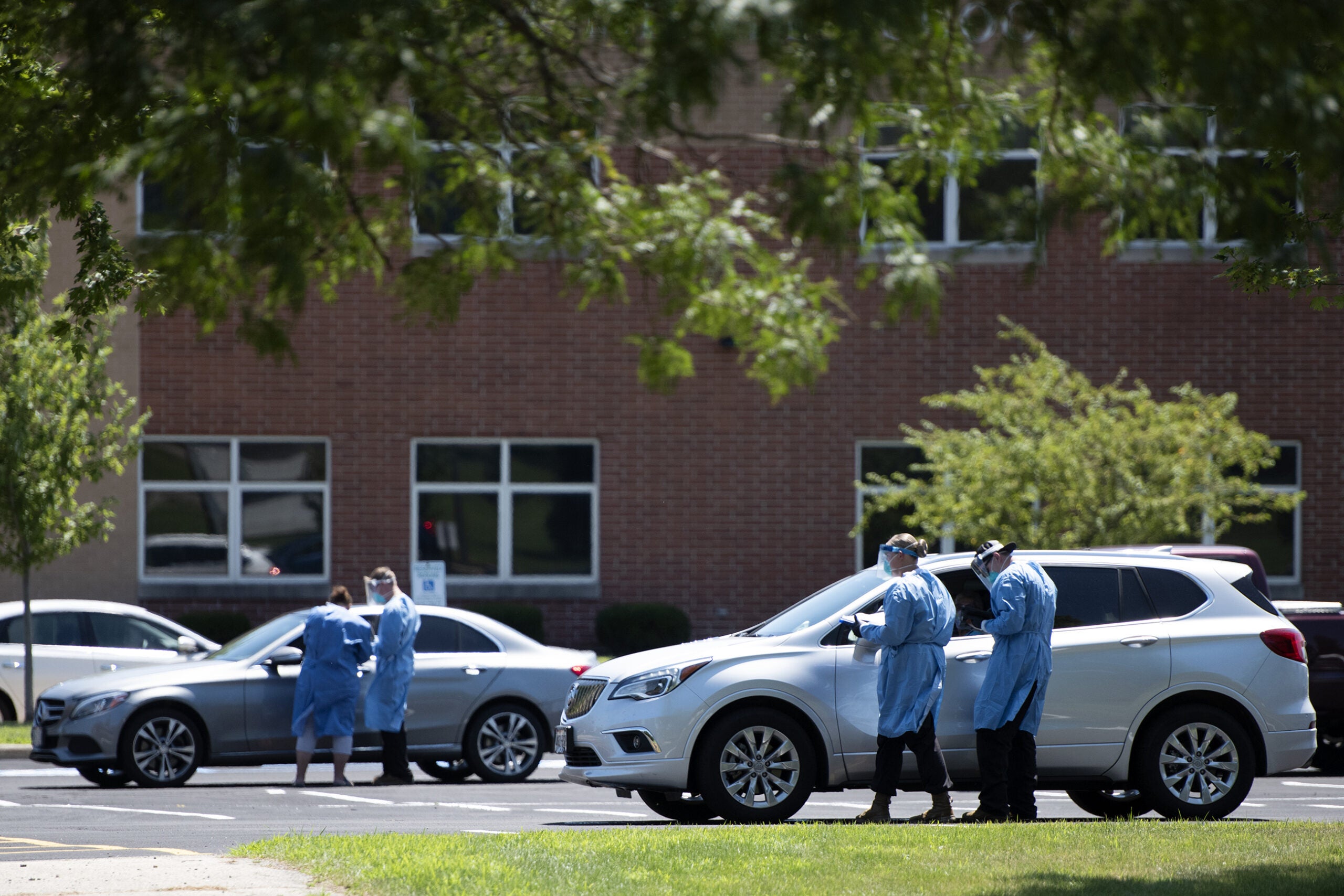 two vehicles in the testing drive thru are approached by people in medical gear