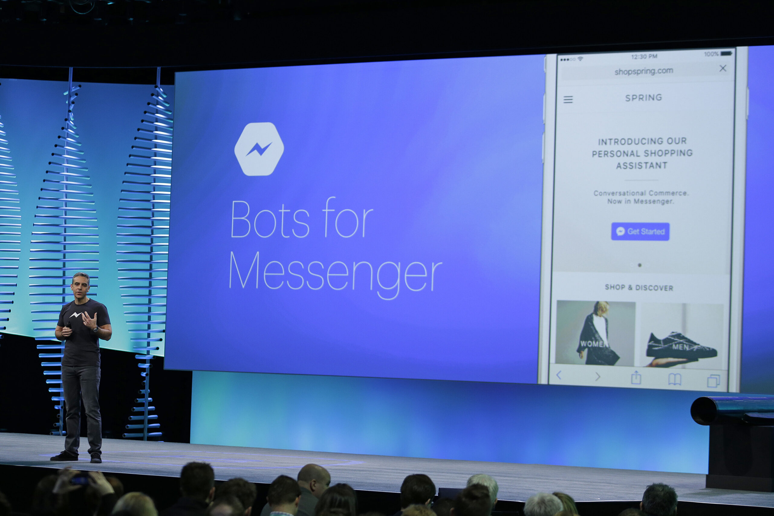 A conference speaker stands in front of a presentation screen talking about the plan for bots on Facebook's messenger app.