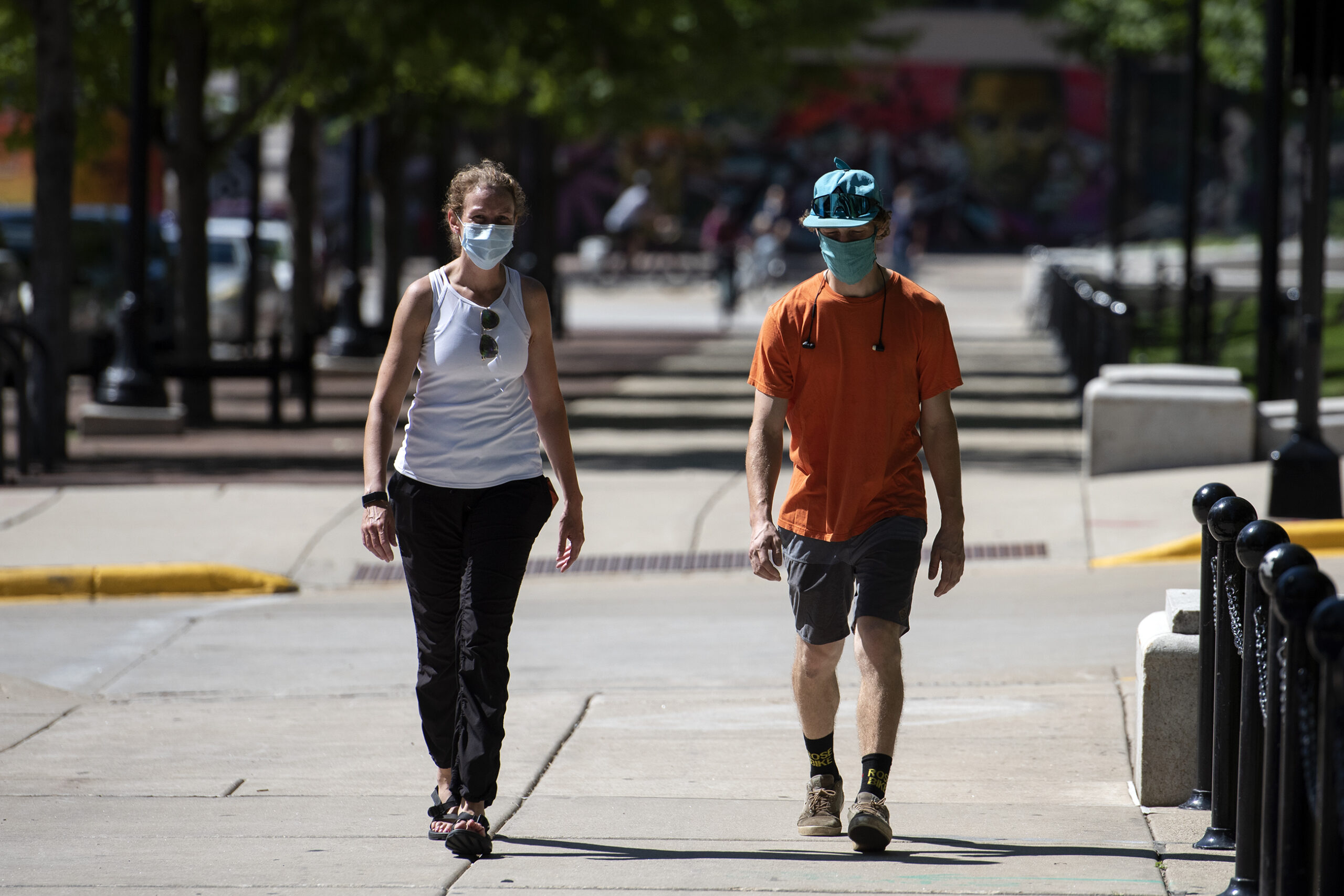 two people walk on a sidewalk near the capitol building in Downtown Madison while wearing masks