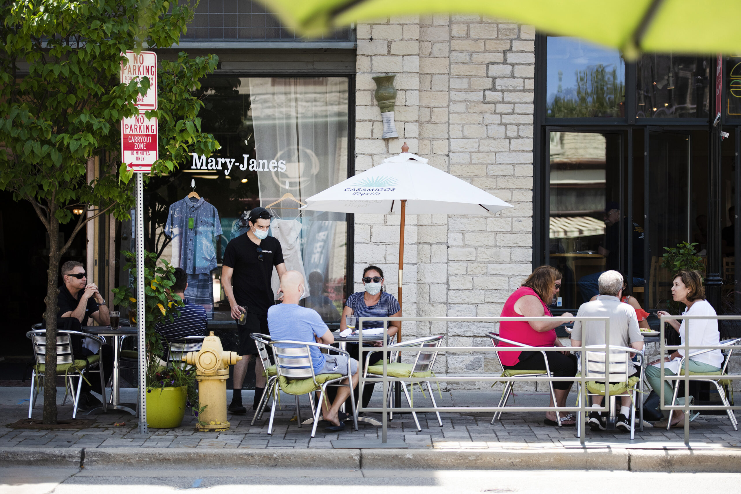 Two people sit at a table while wearing masks as those around them do not