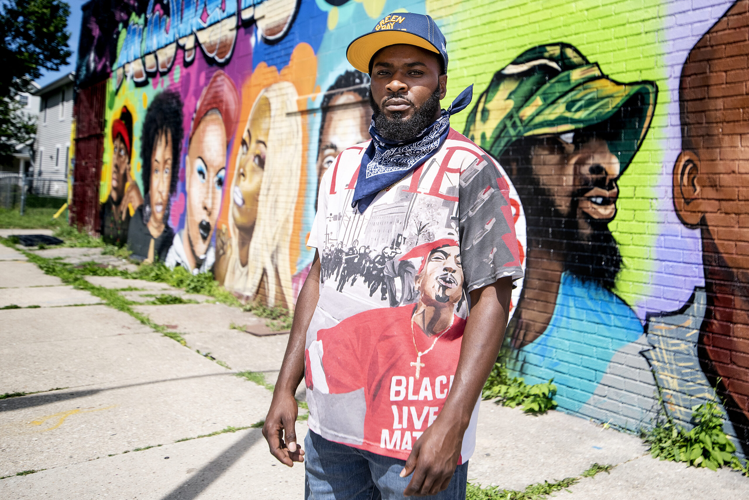 A man stands in front of a colorful mural showing the faces of people involved in the black lives matter movement