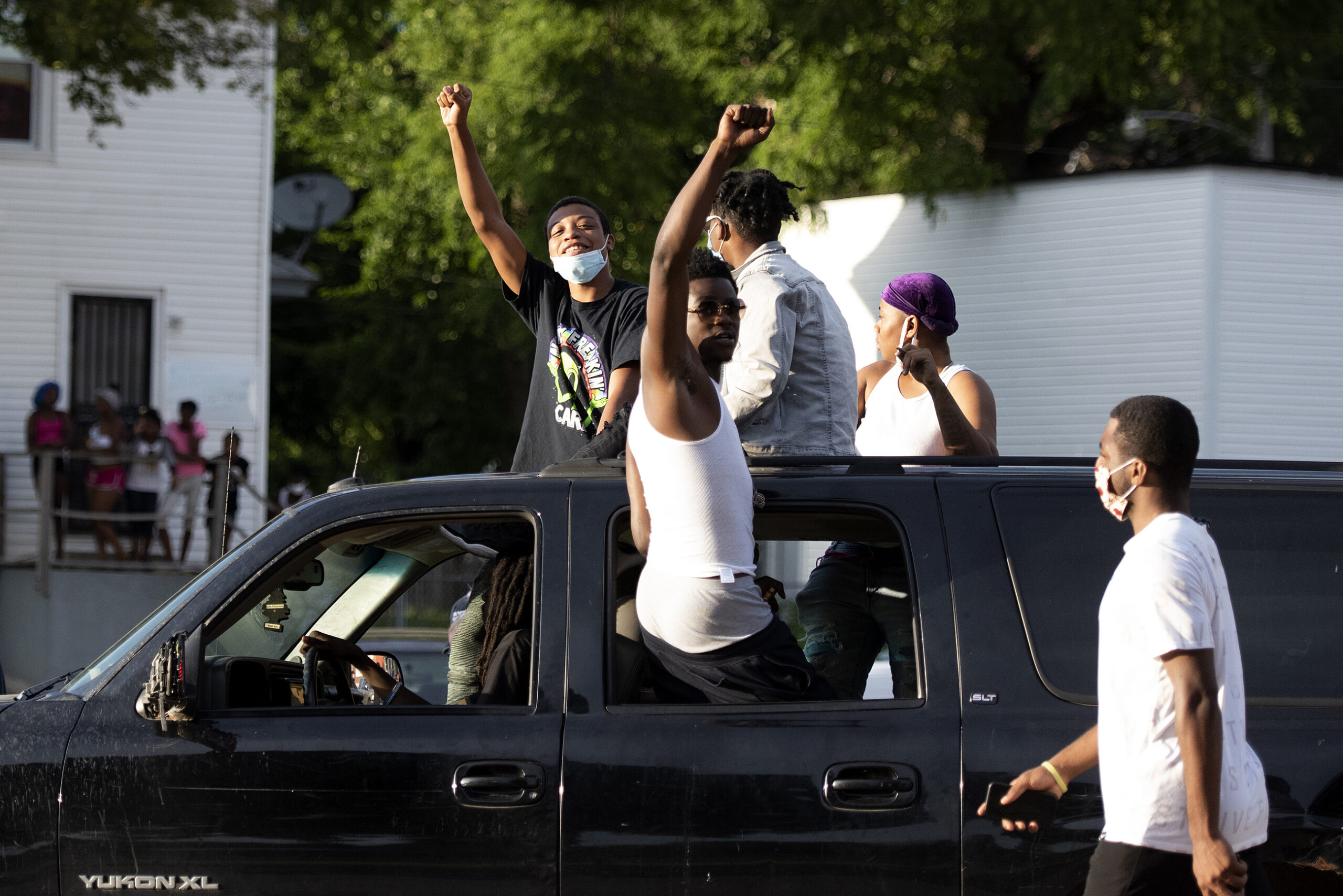 Two people seated on a SUV's open window raise their fists