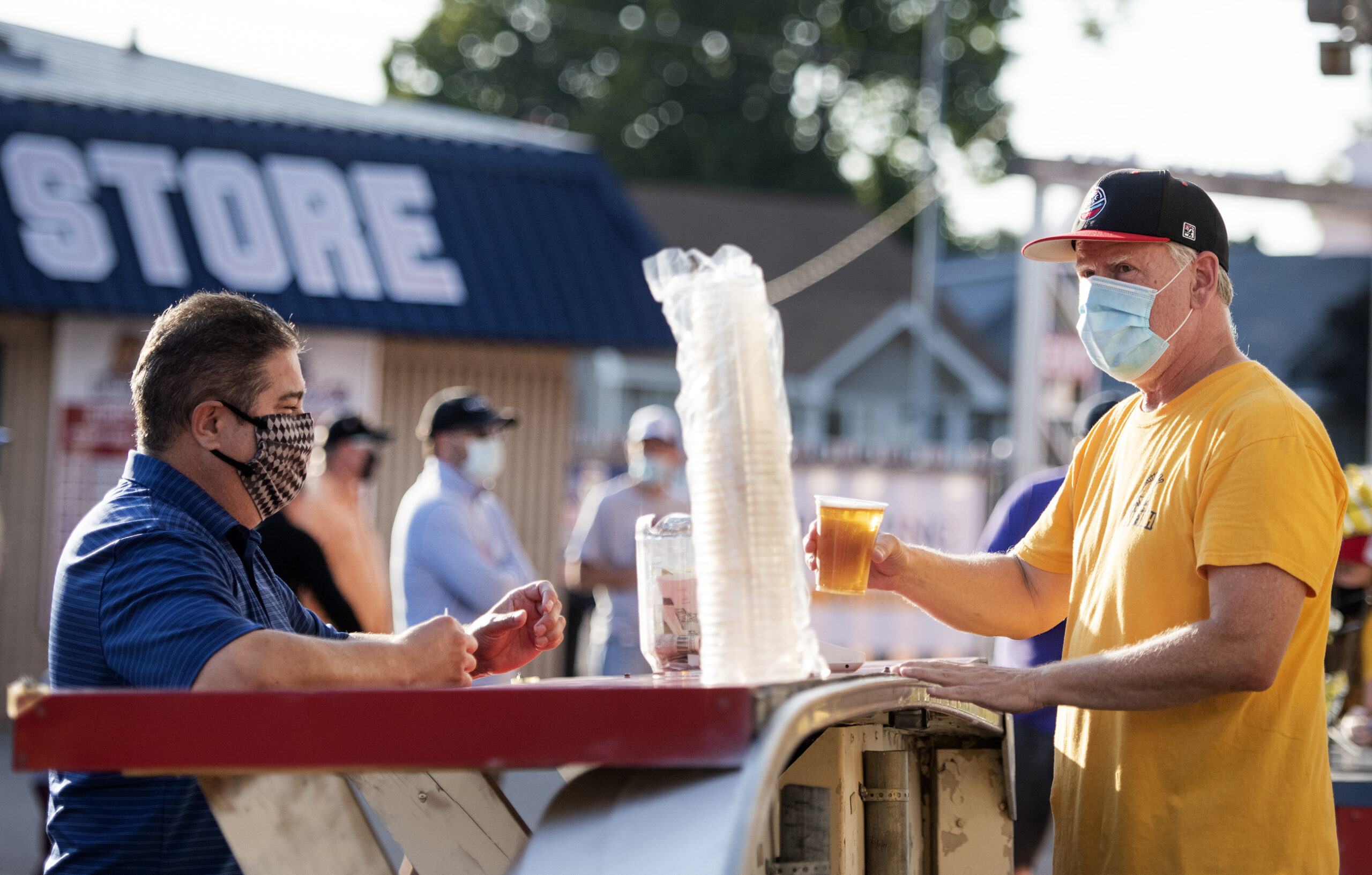 a man in a mask serves beer at an outdoor tap to a customer in a mask