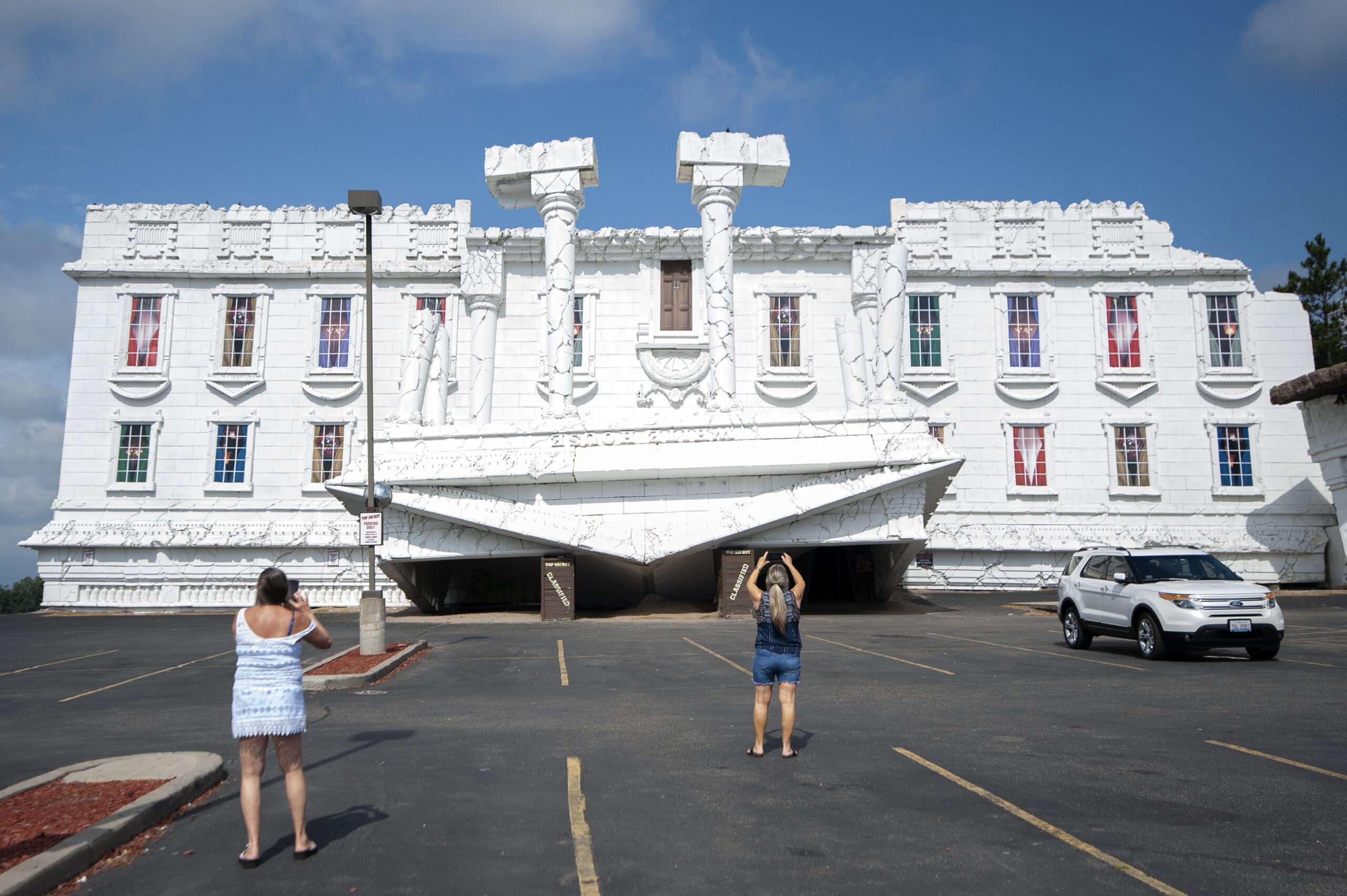 two people can be seen from behind taking photos in a parking lot of the upside down White House in the dells