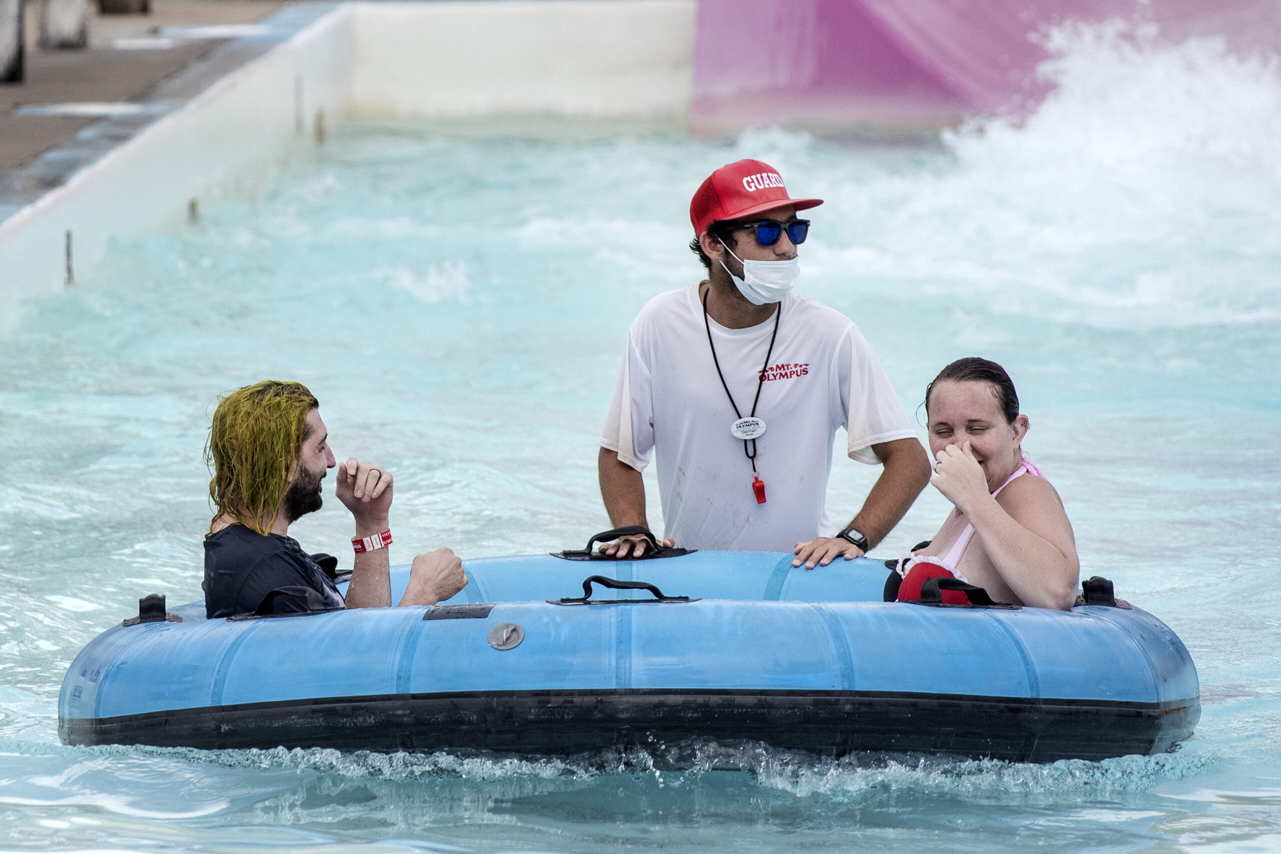 two people in a raft are pushed by a worker in a face mask at the bottom of a water slide