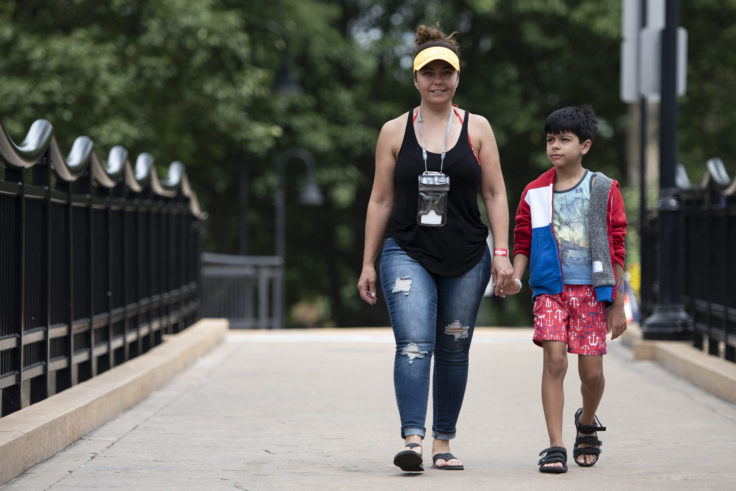 a mother and son hold hands as they walk on a riverwalk