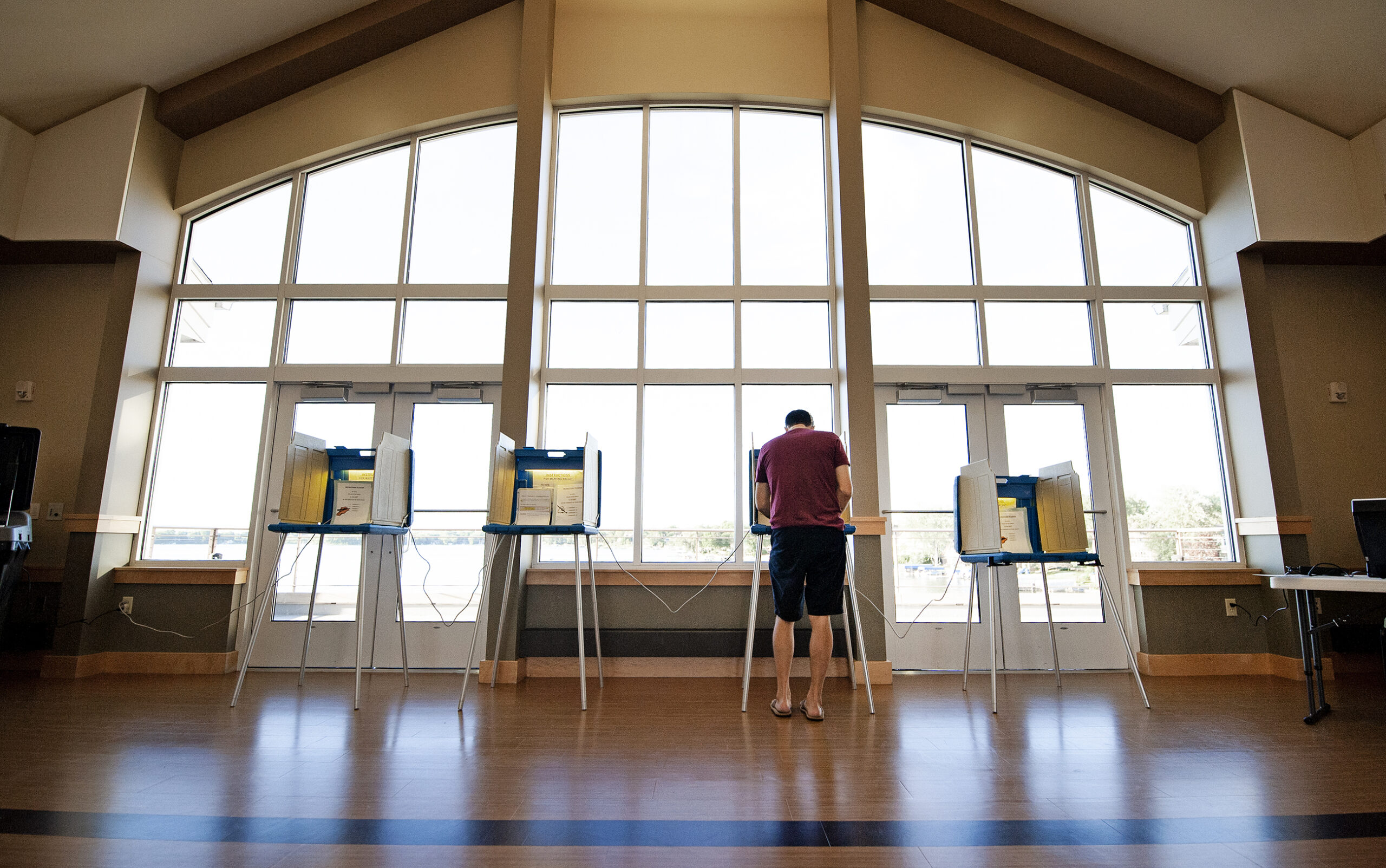 a voter is seen from behind as he votes at one of four available voting stations in front of a large window
