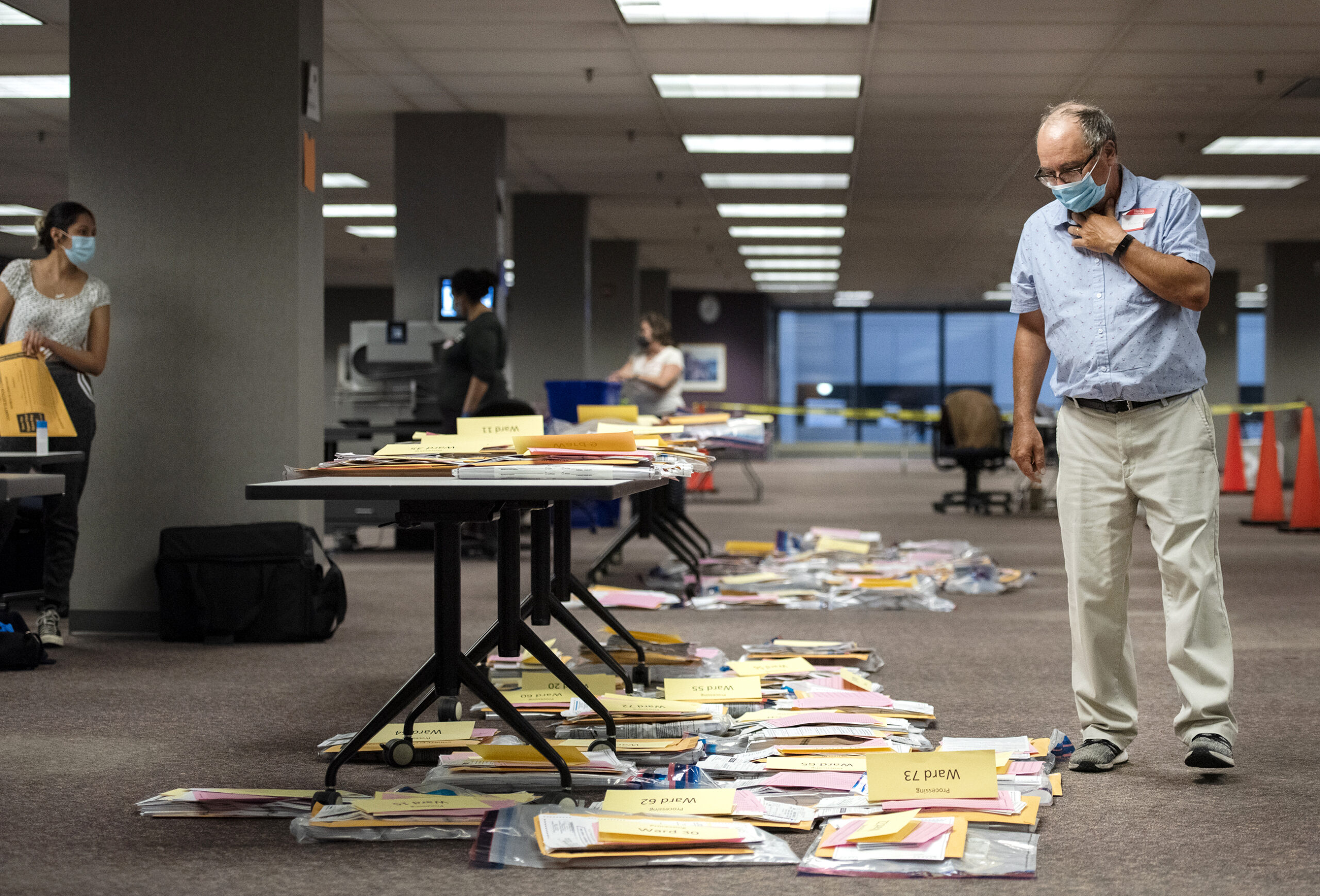 a man in a face mask walks by ballots placed on the floor and on a table