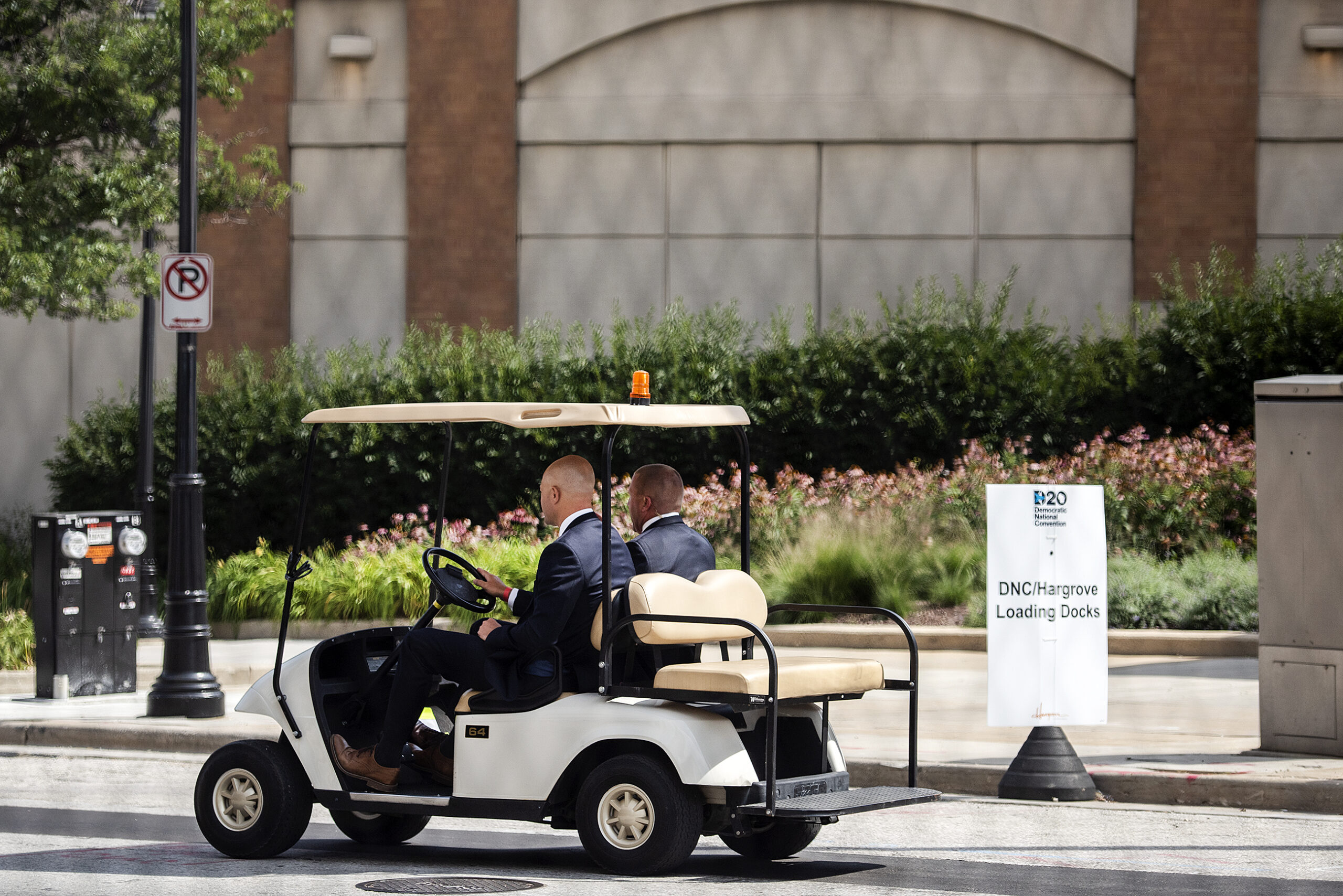 two bald men in suits ride in a golf cart