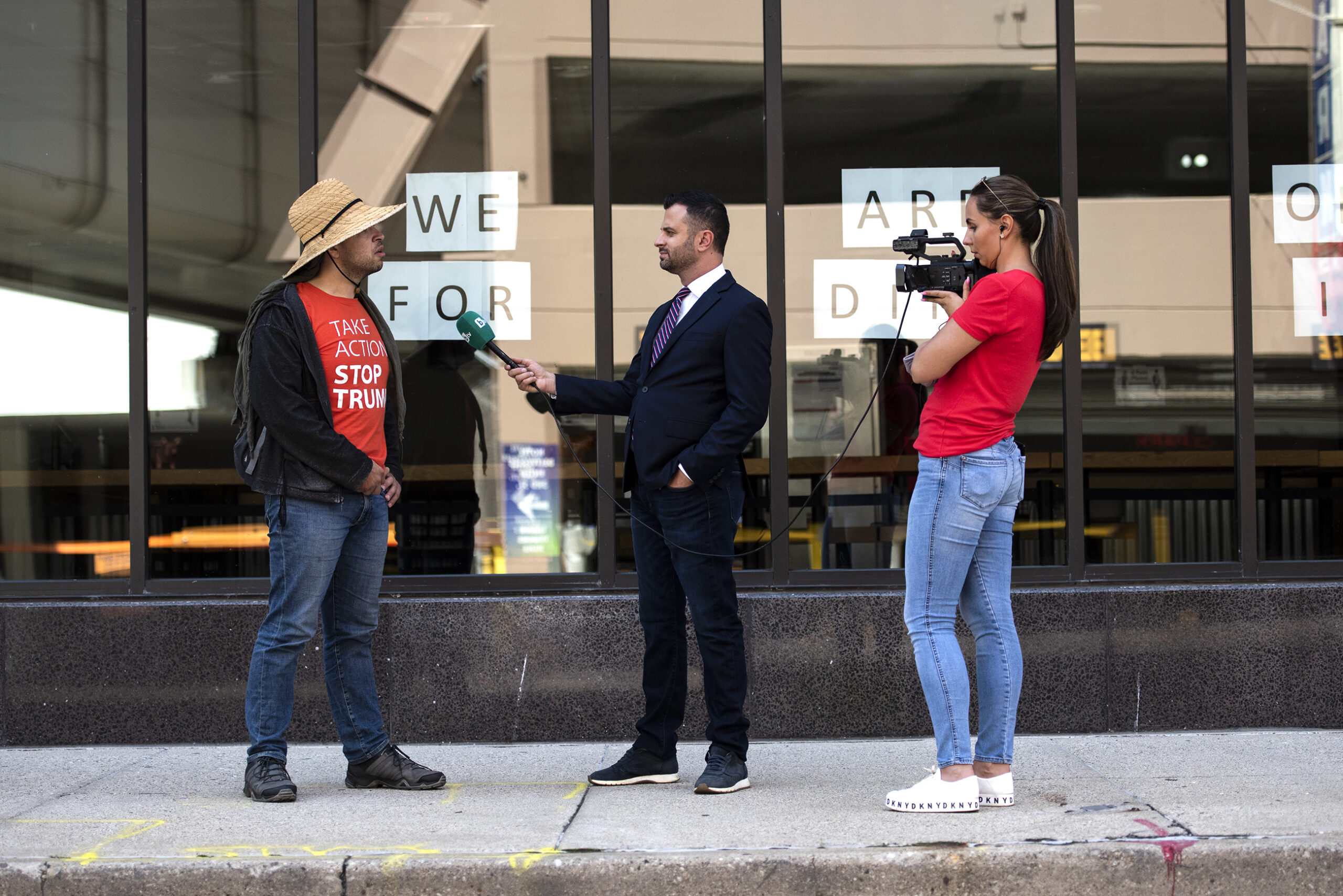 a man in a suit holds up a microphone to a person on a sidewalk