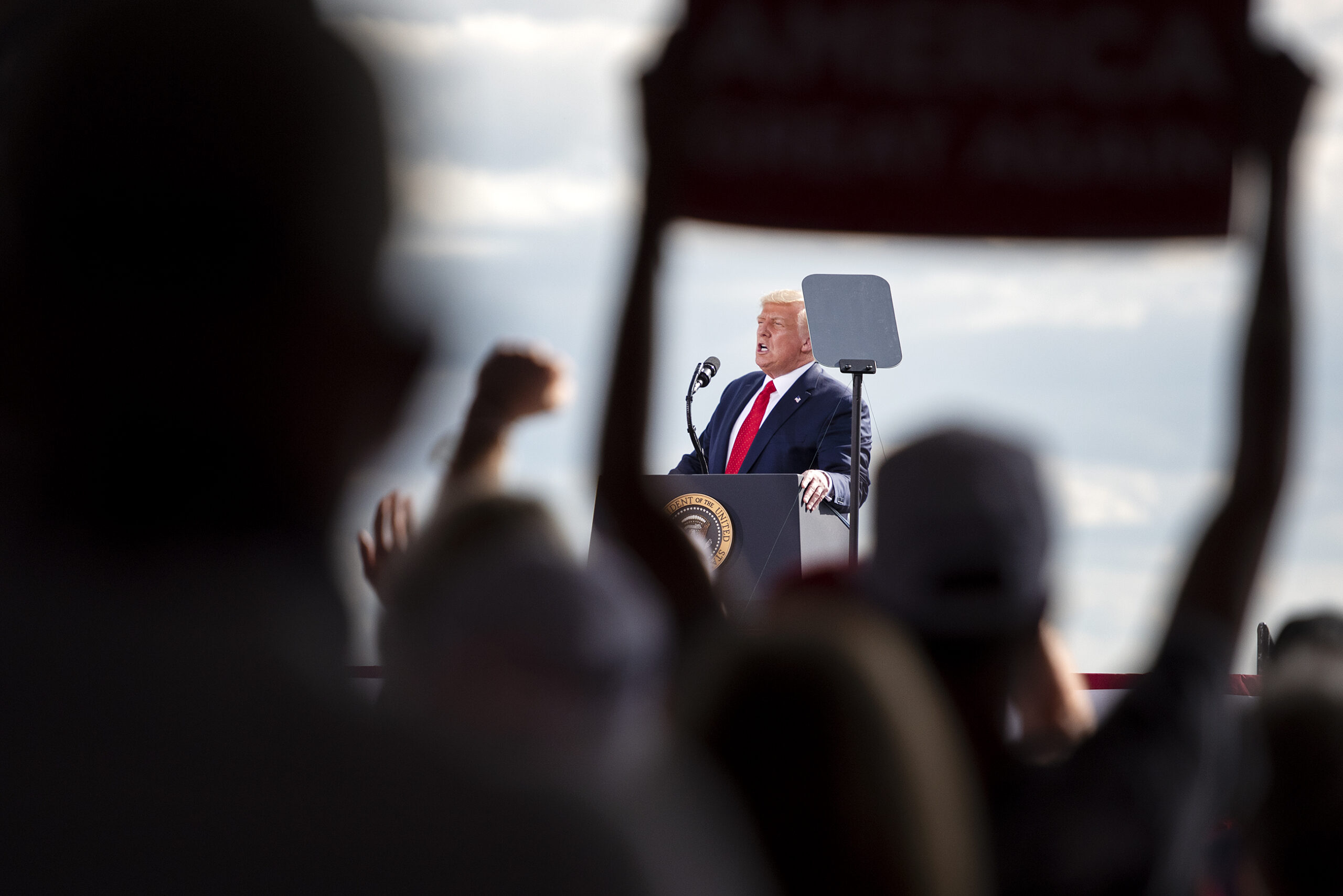 President Donald Trump can be seen through two arms holding up a sign in the crowd