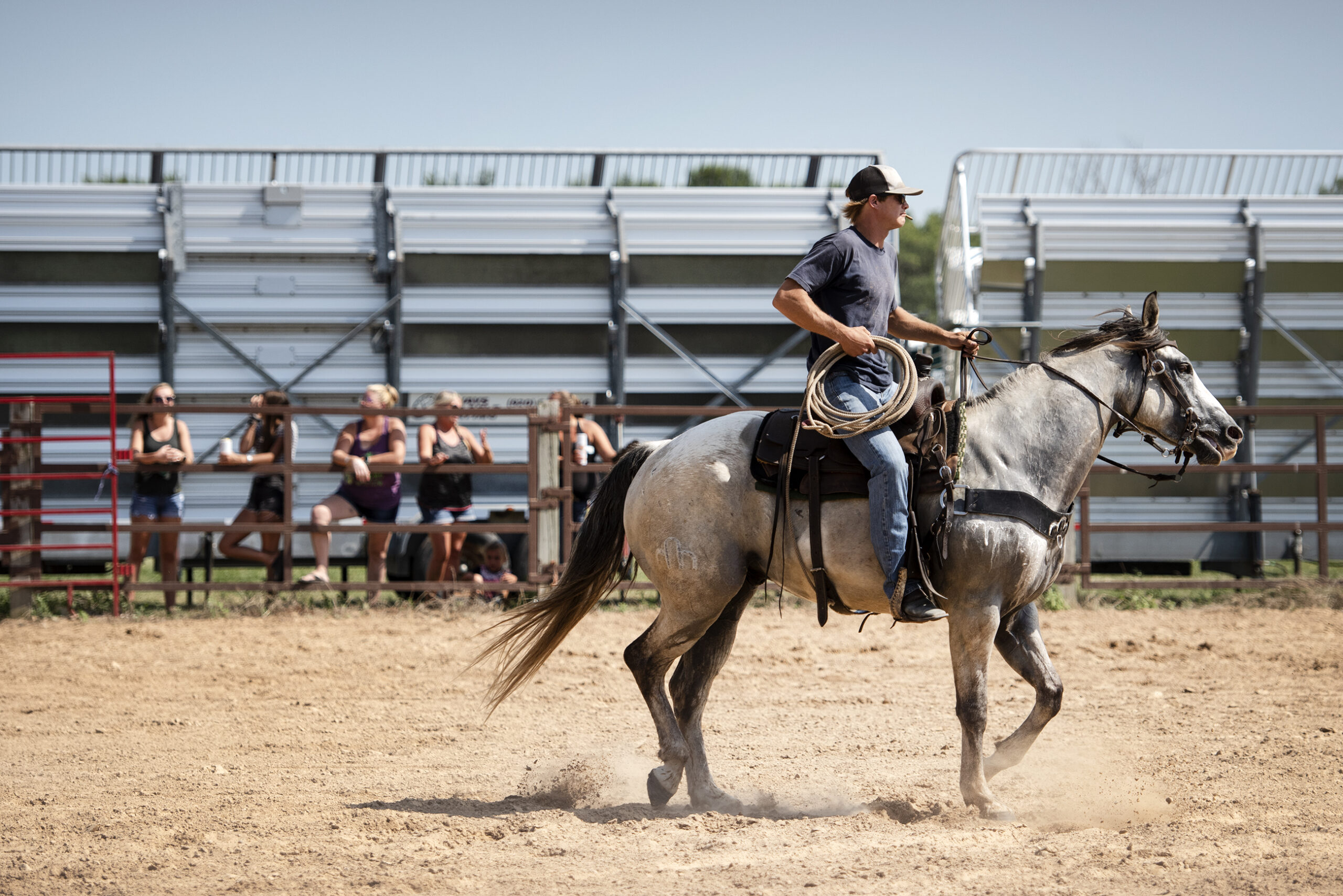 A man riding a horse holds a rope as he rides on a dirt arena