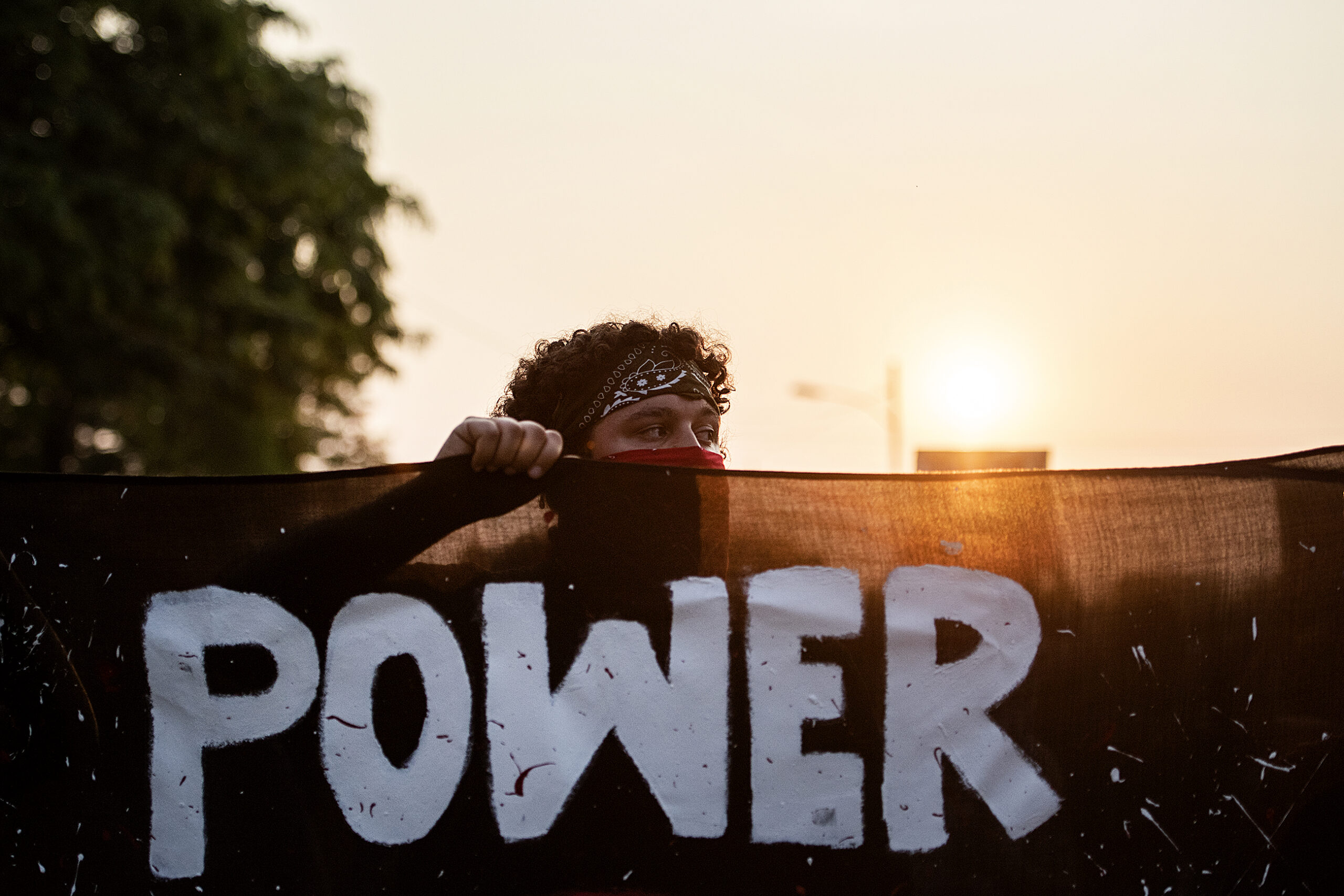 A protester holds a banner with the word "power" as the sun sets behind him