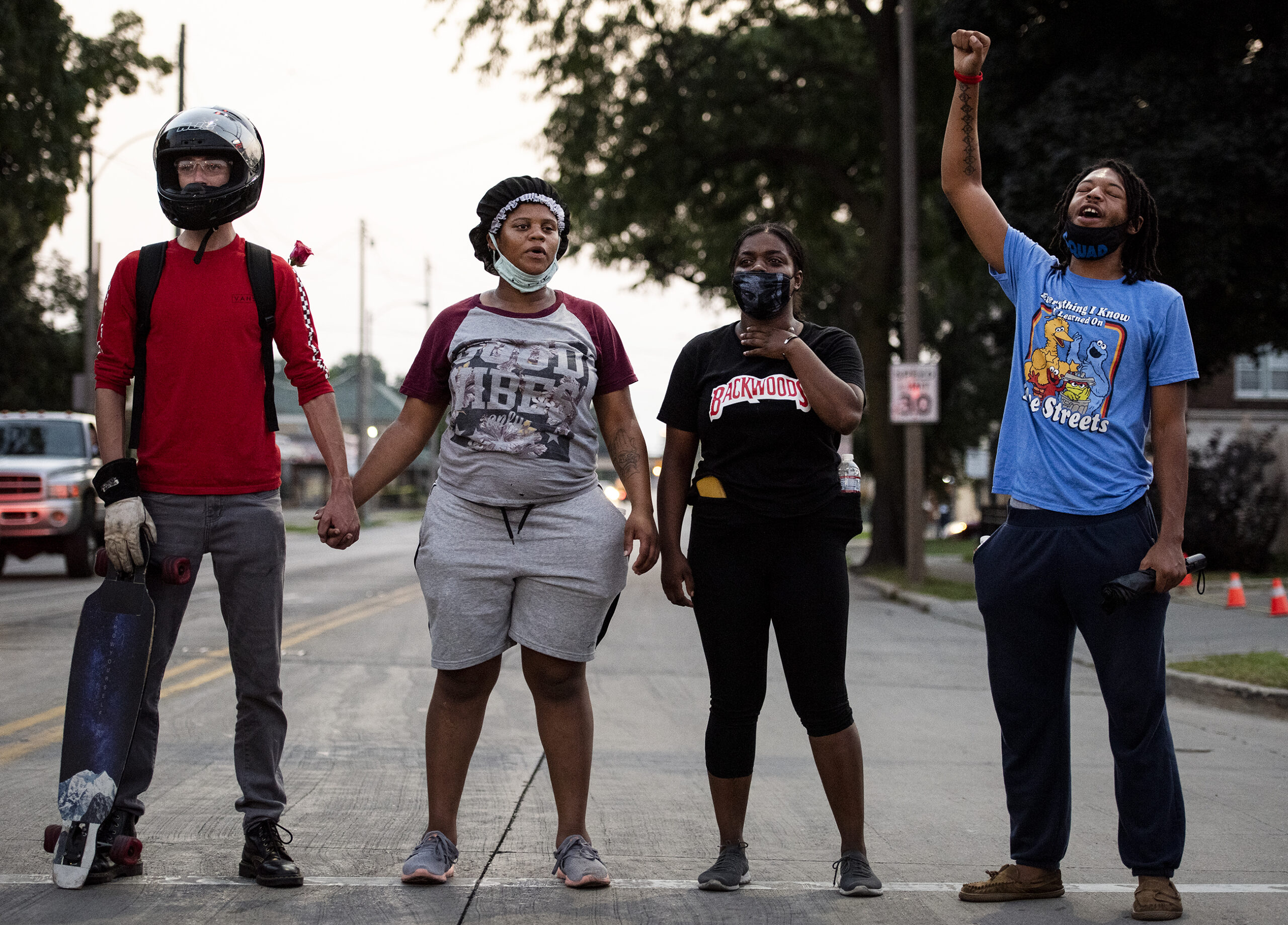 four people hold hands and raise their fists as they stand in the road