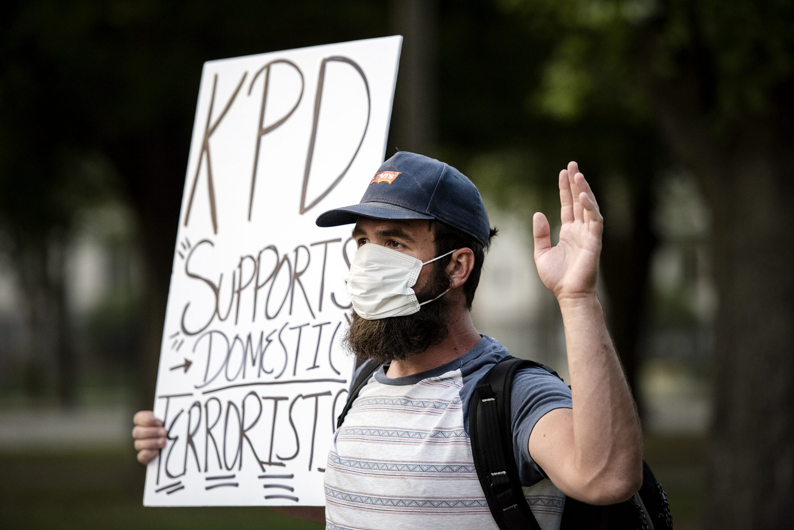 a protester with a sign that says "KPD supports domestic terrorists" holds up his hand