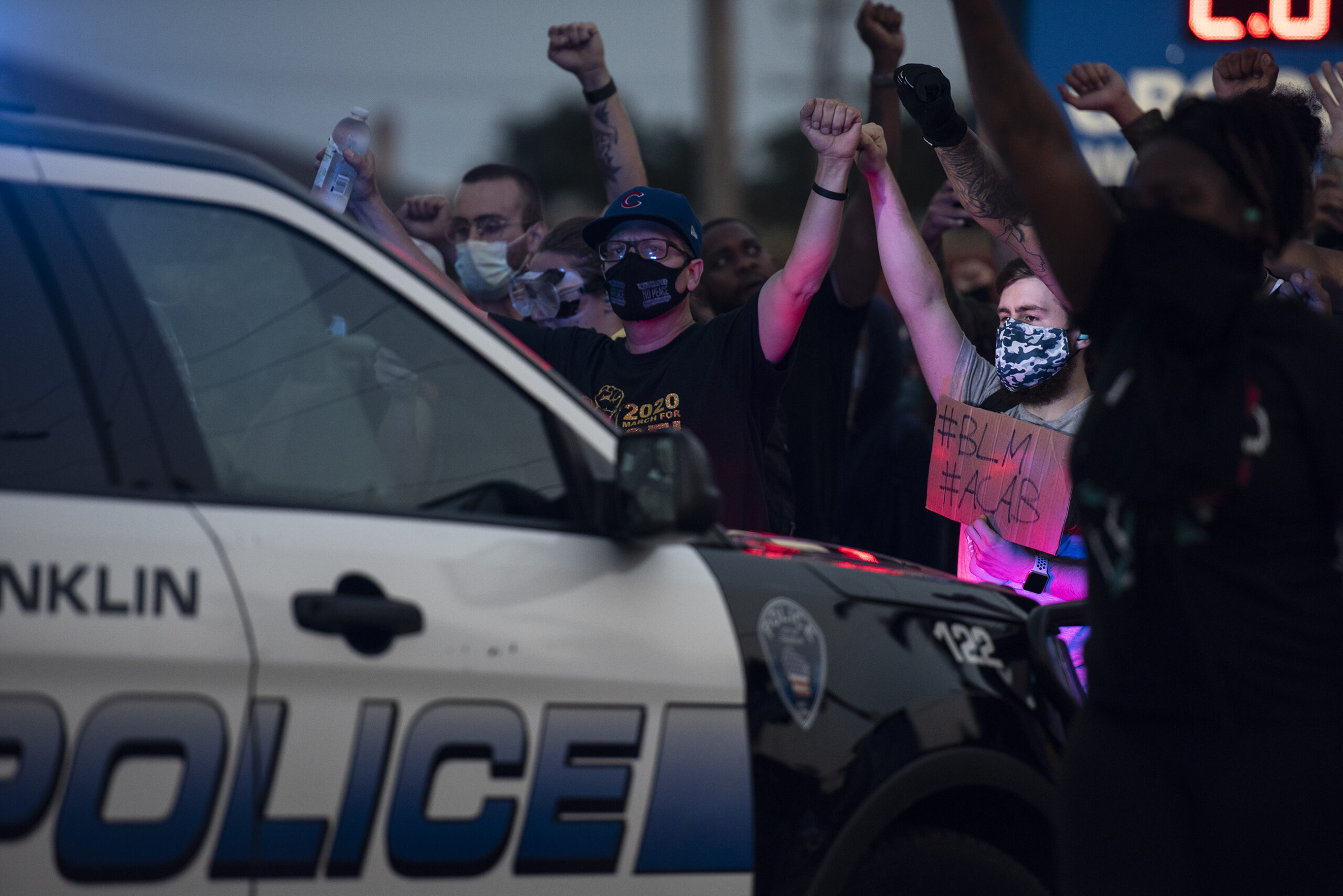 Protesters are illuminated by police lights as they raise their fists