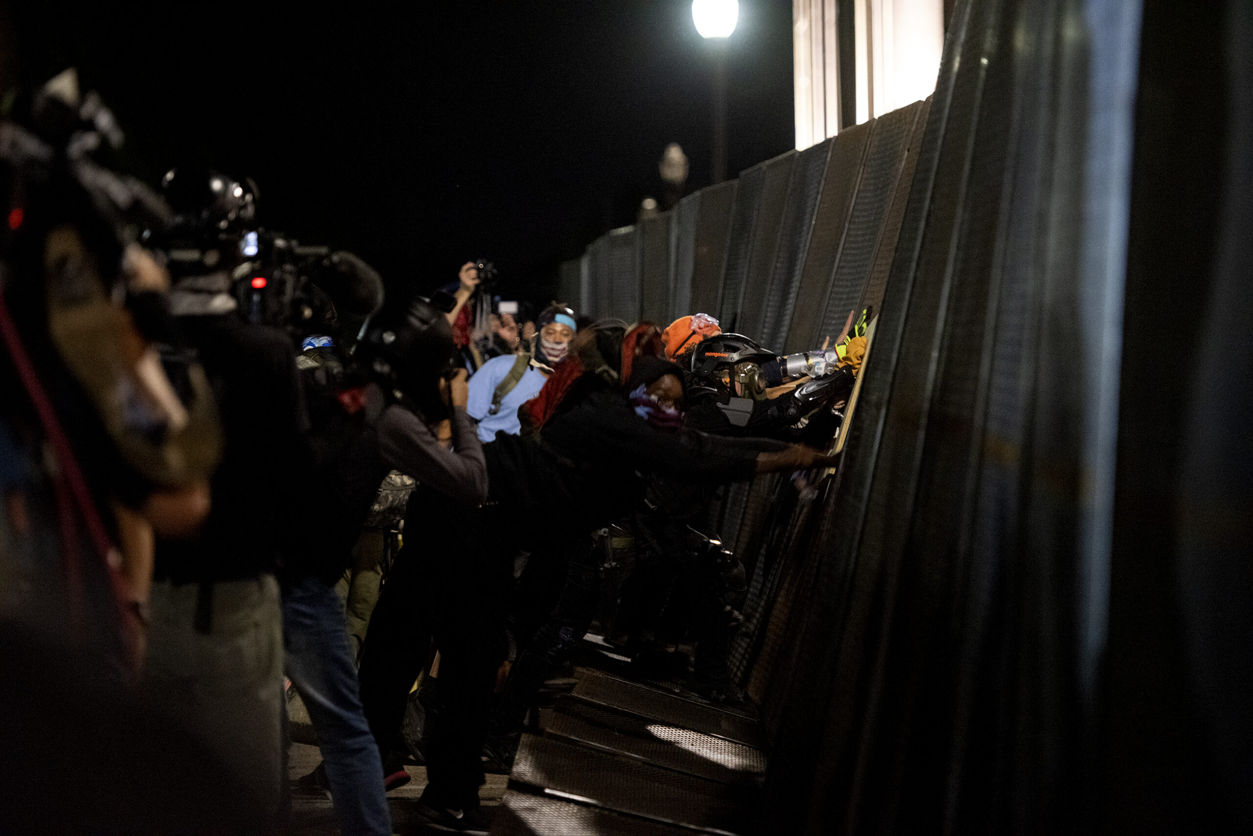a large black fence bends slightly as protesters push on it