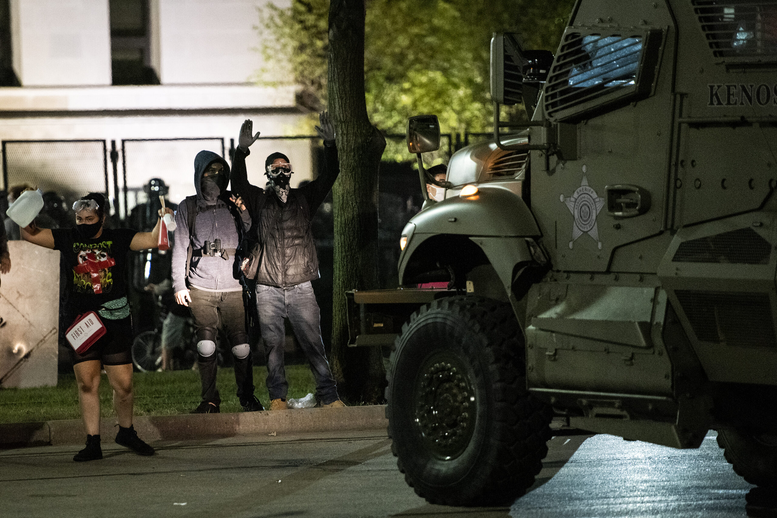 a headlight shines on protesters, one has their hands raised