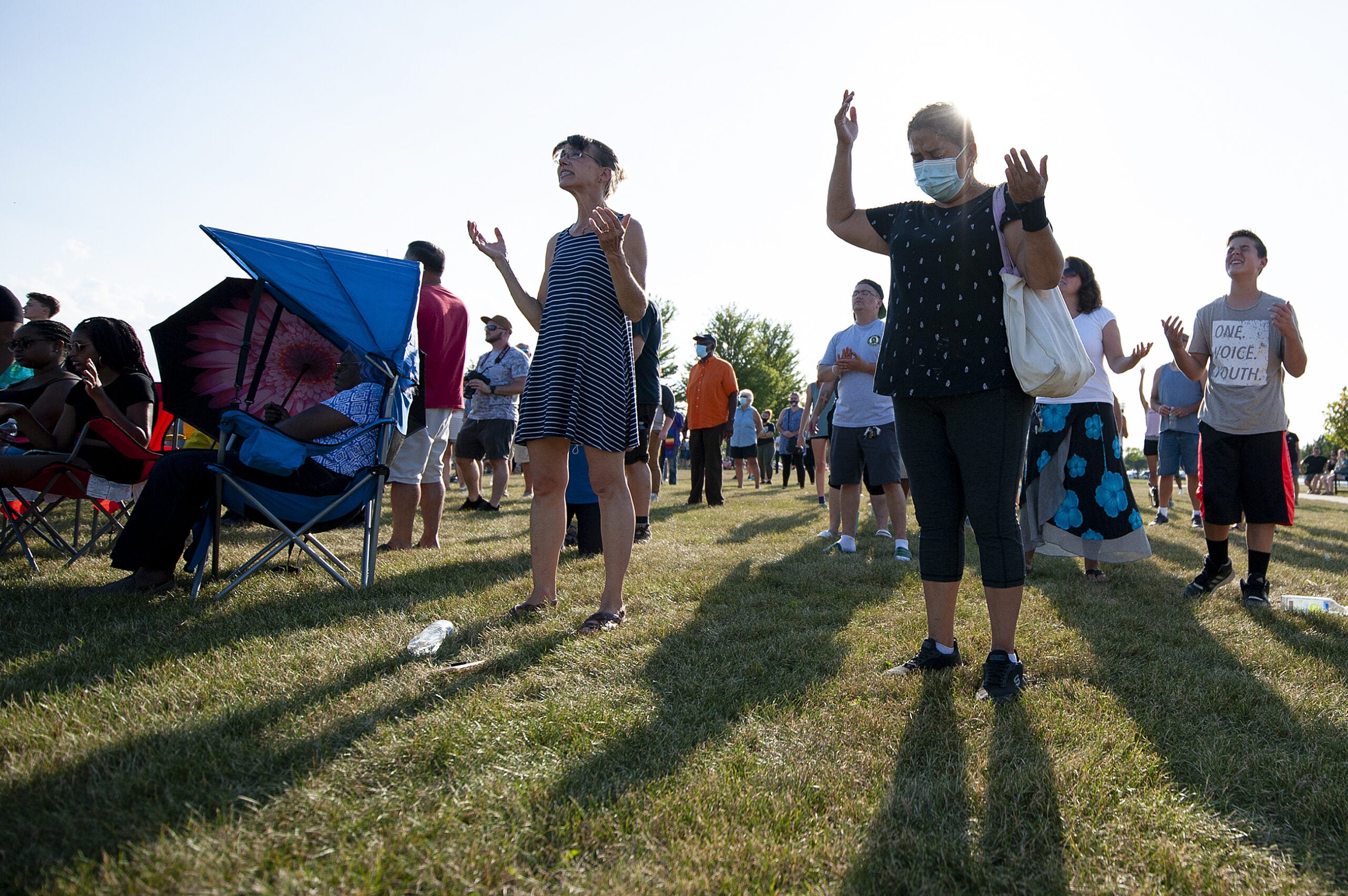 two women hold their hands up as they stand outside on the grass. the sun shines behind them.