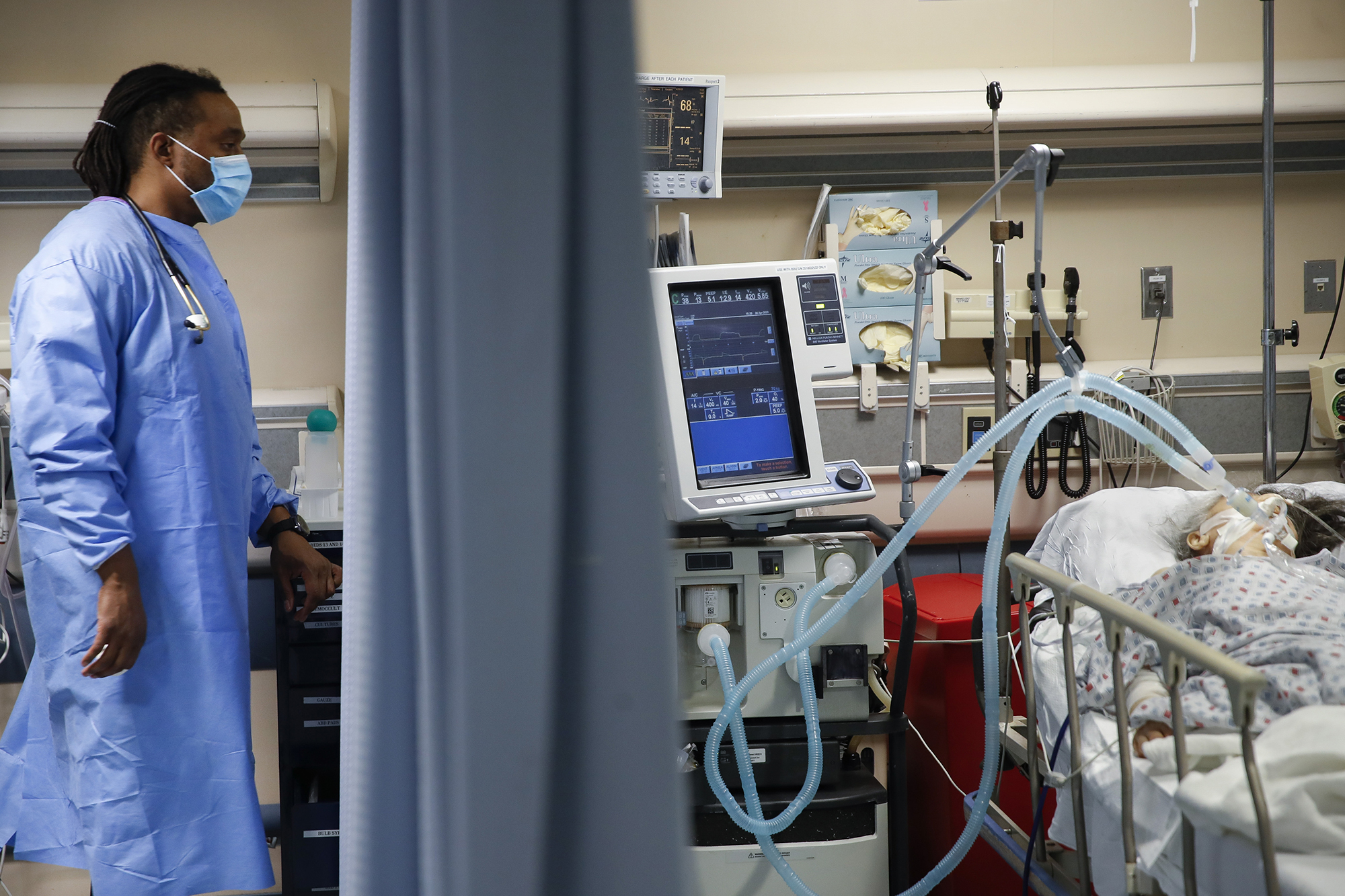 A nurse looks over at a COVID-19 patient who is attached to a ventilator