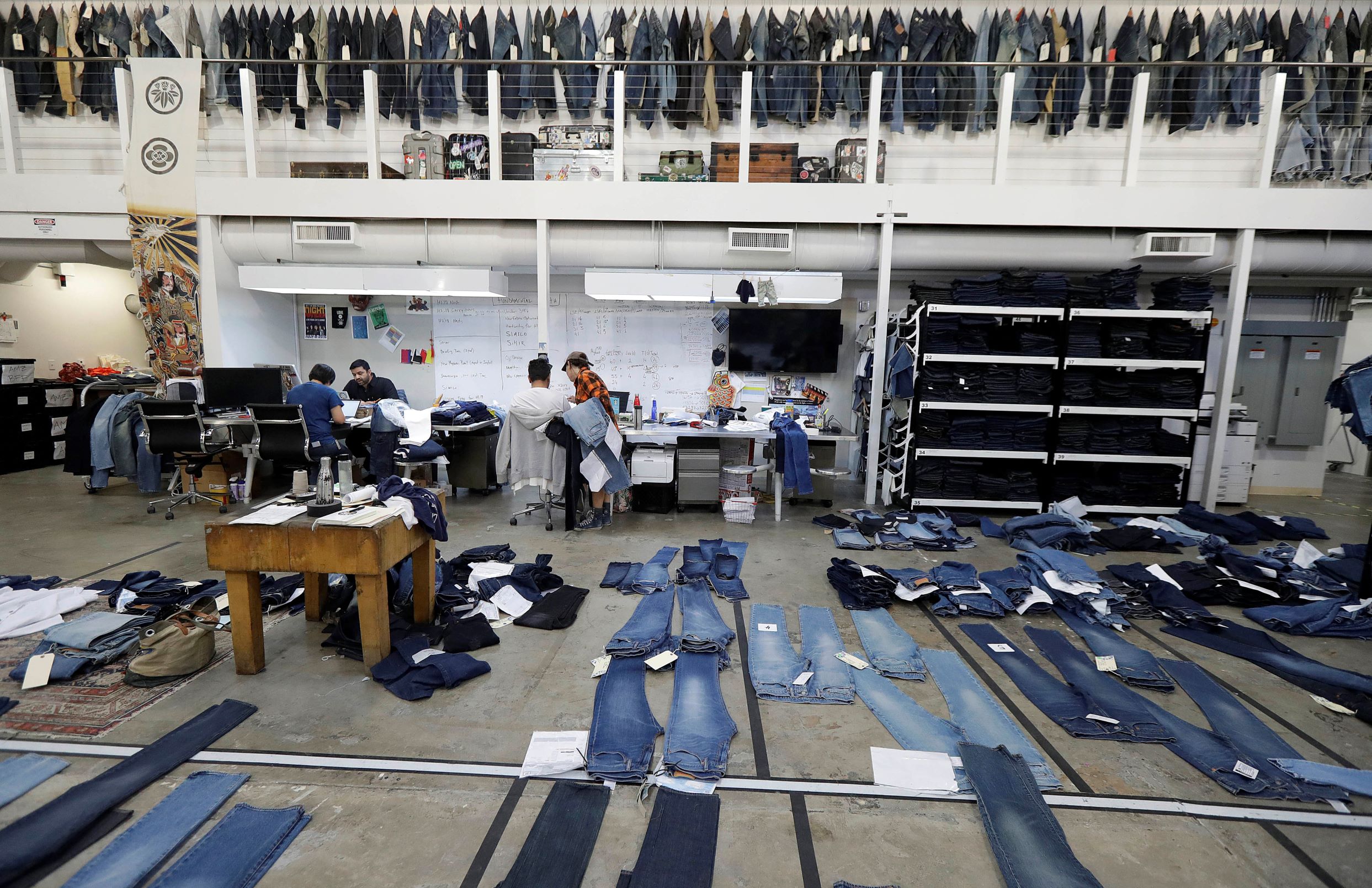Several pairs of jeans are laid out on the floor of an open studio work space.