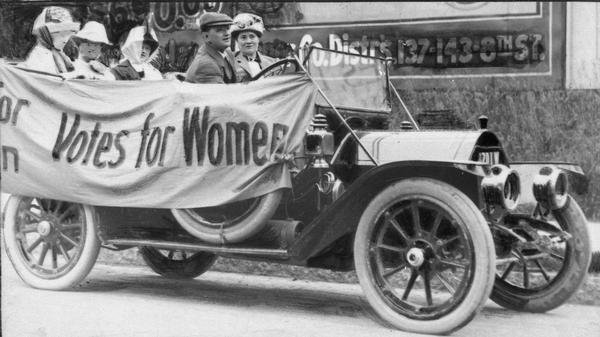 Suffragists in a vehicle with a sign reading "Votes for Women"