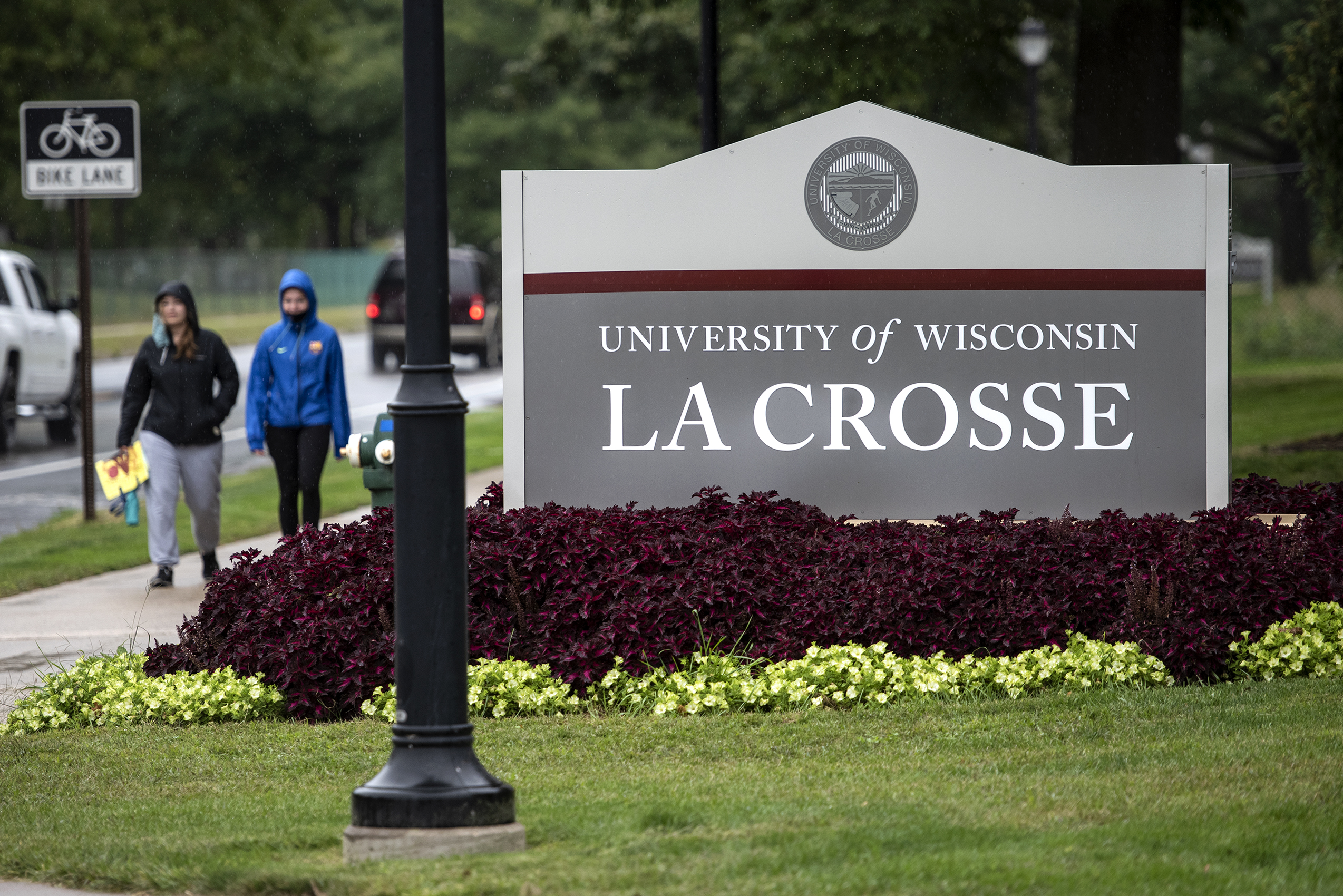 People walk by a sign that says "University of Wisconsin La Crosse"