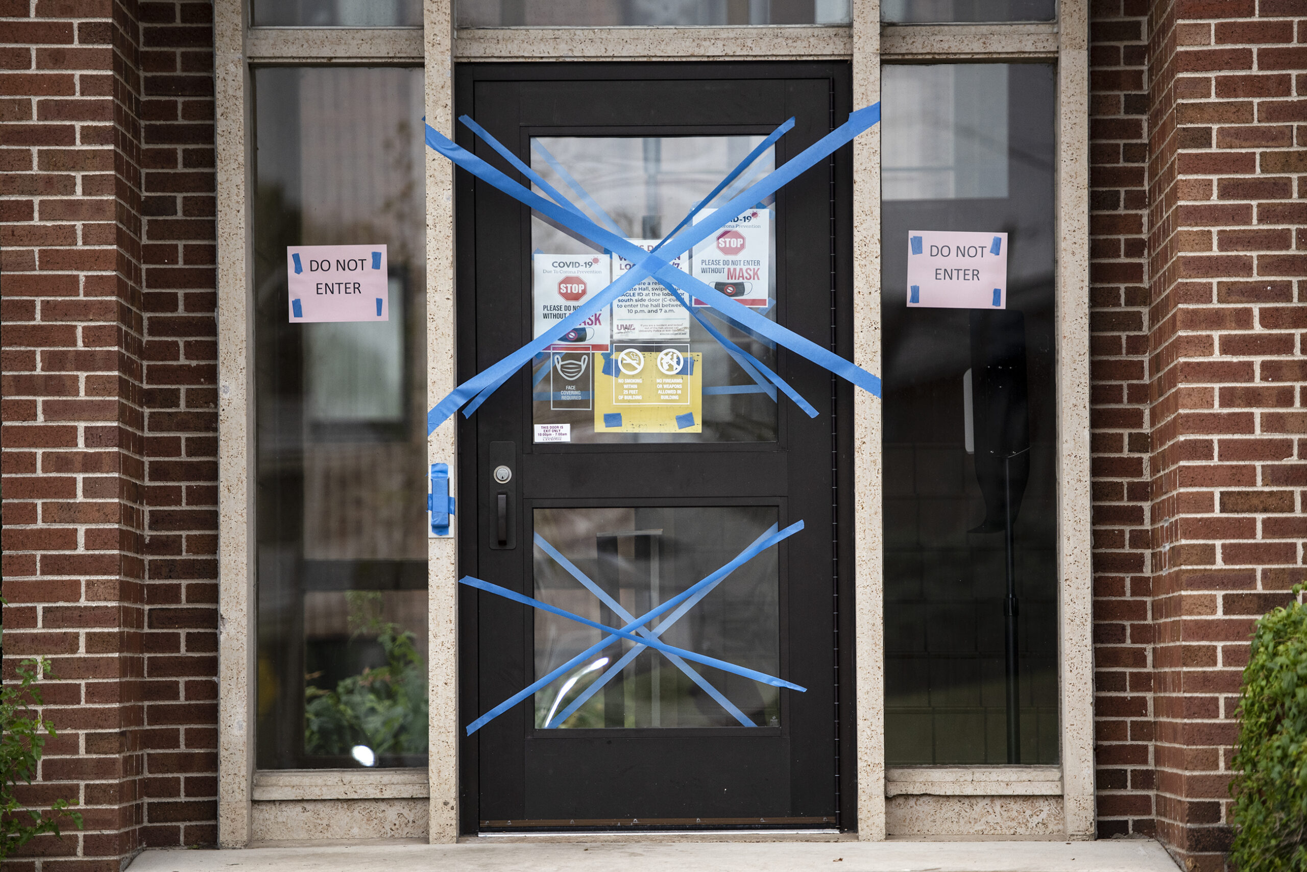 Blue painter's tape blocks off a doorway. several signs indicate that people should not enter.