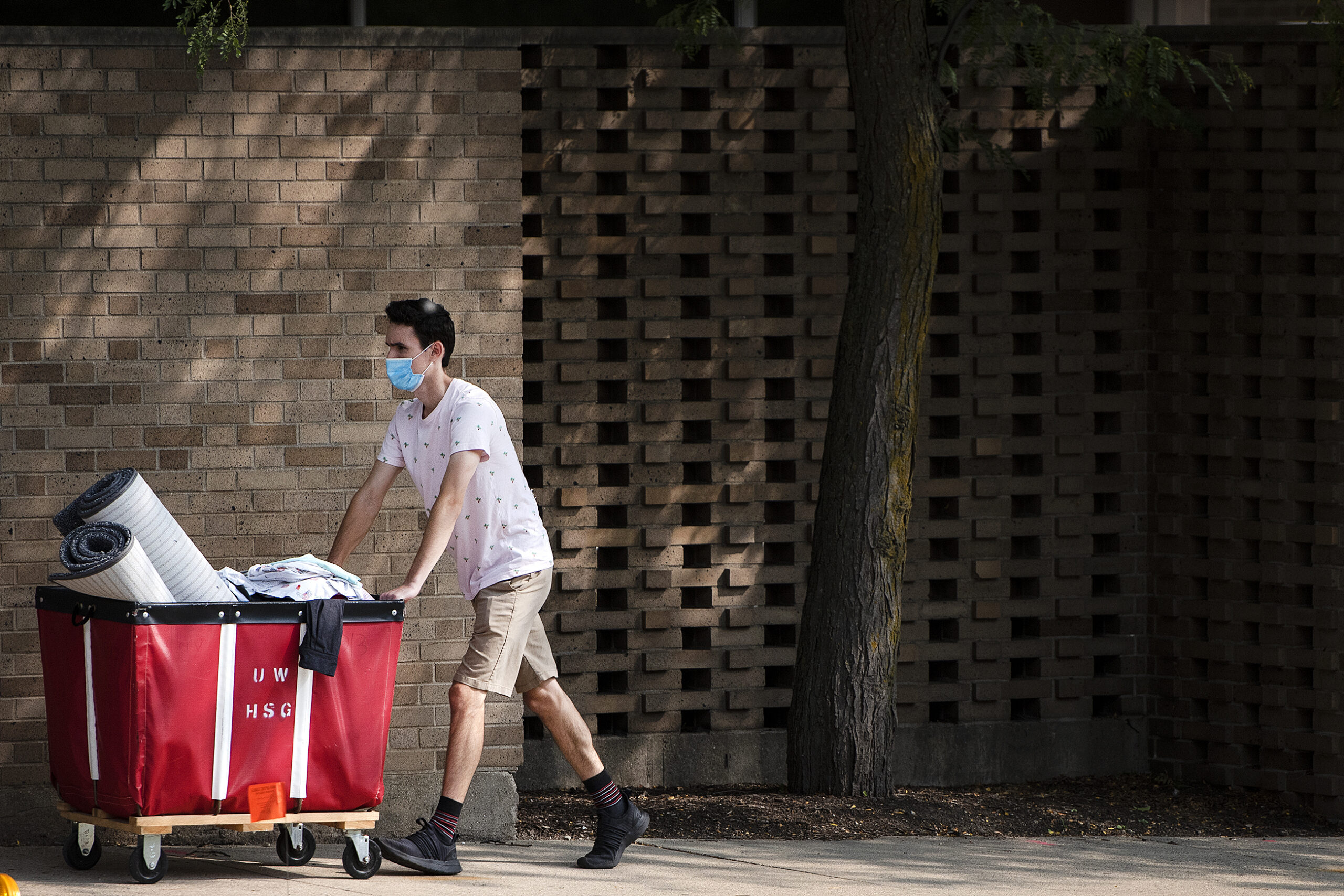 a student pushes a red bin with his belongings on a sidewalk outside sellery dormitory