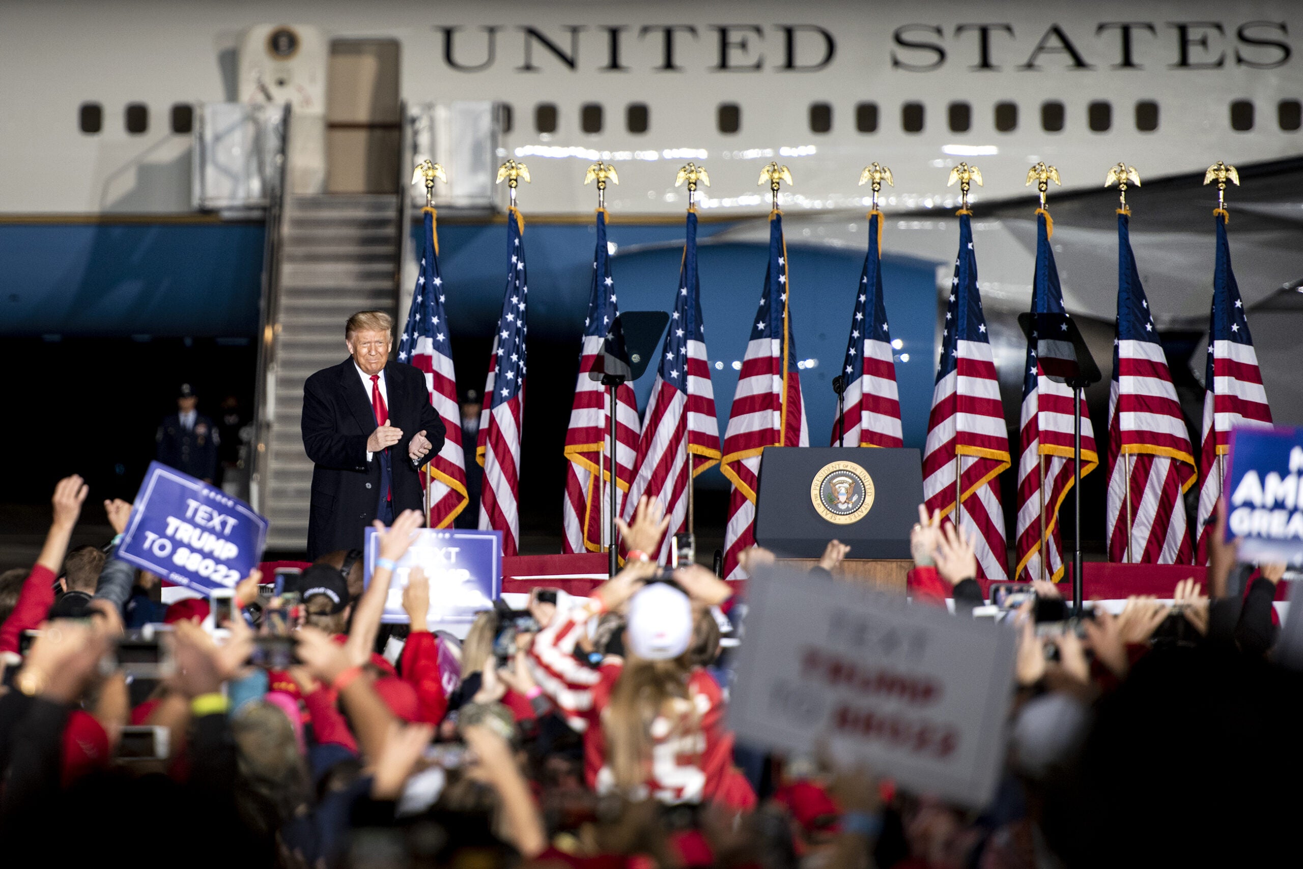 Air Force One can be seen behind Pres. Trump as he walks on stage