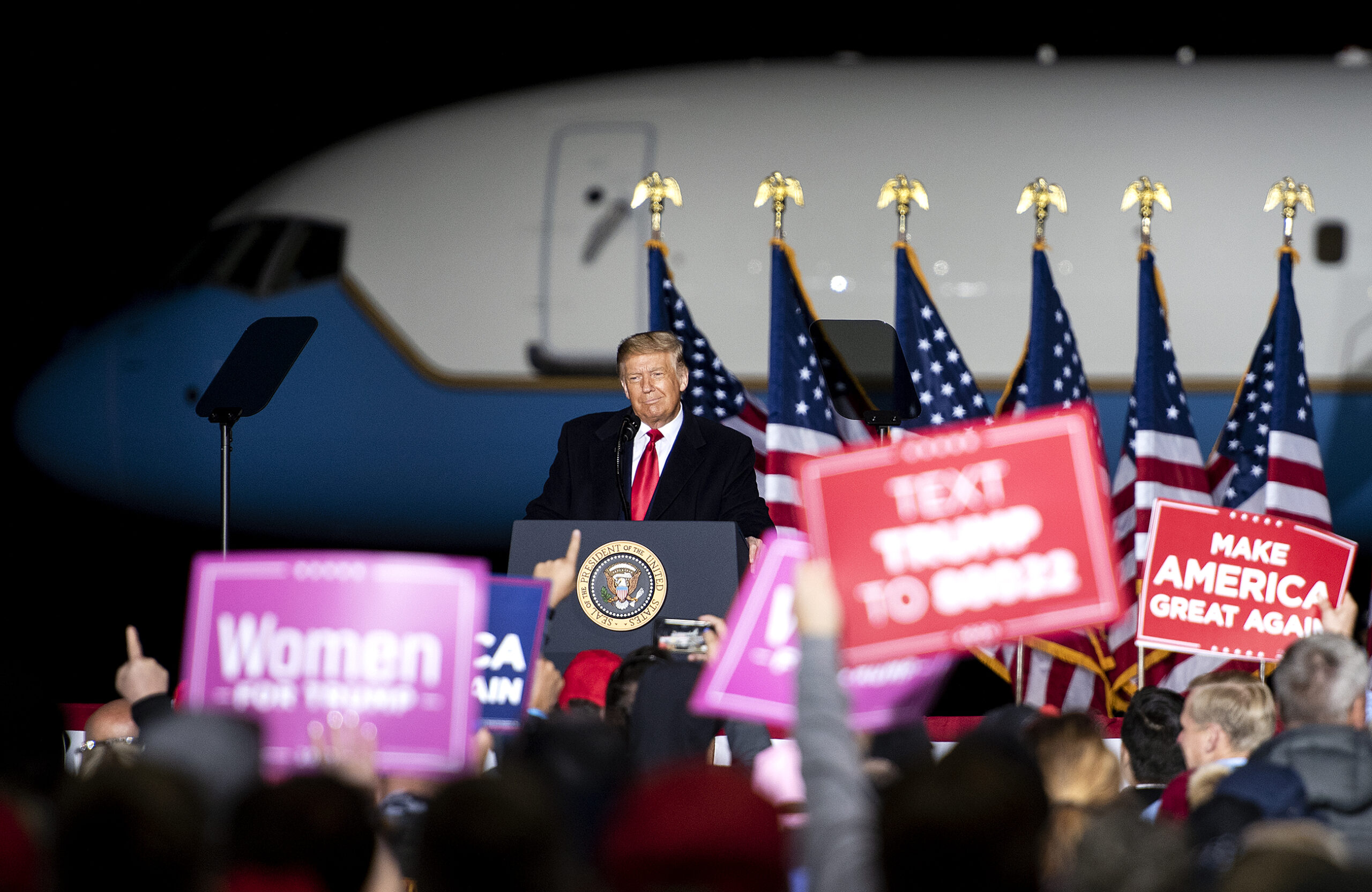 President Trump stands in front of Air Force One and a dark night sky as his supporters wave red and pink signs in the crowd