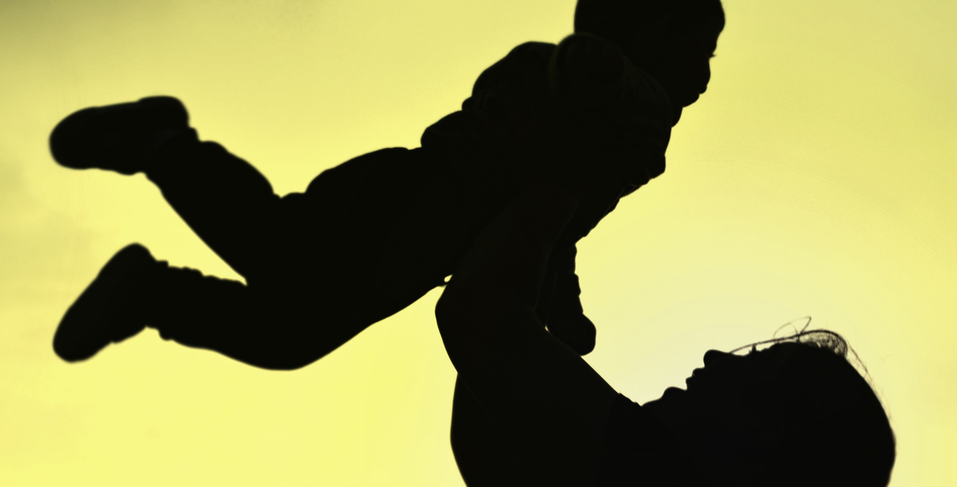 Silhouette of woman holding up child.