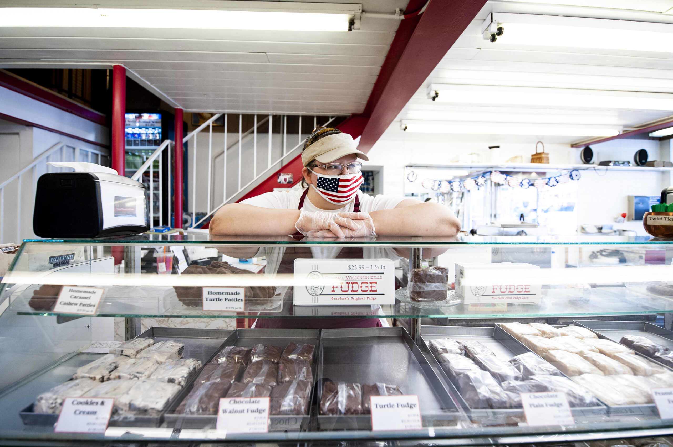 a woman in an American flag face mask puts her arms up on a display of fudge
