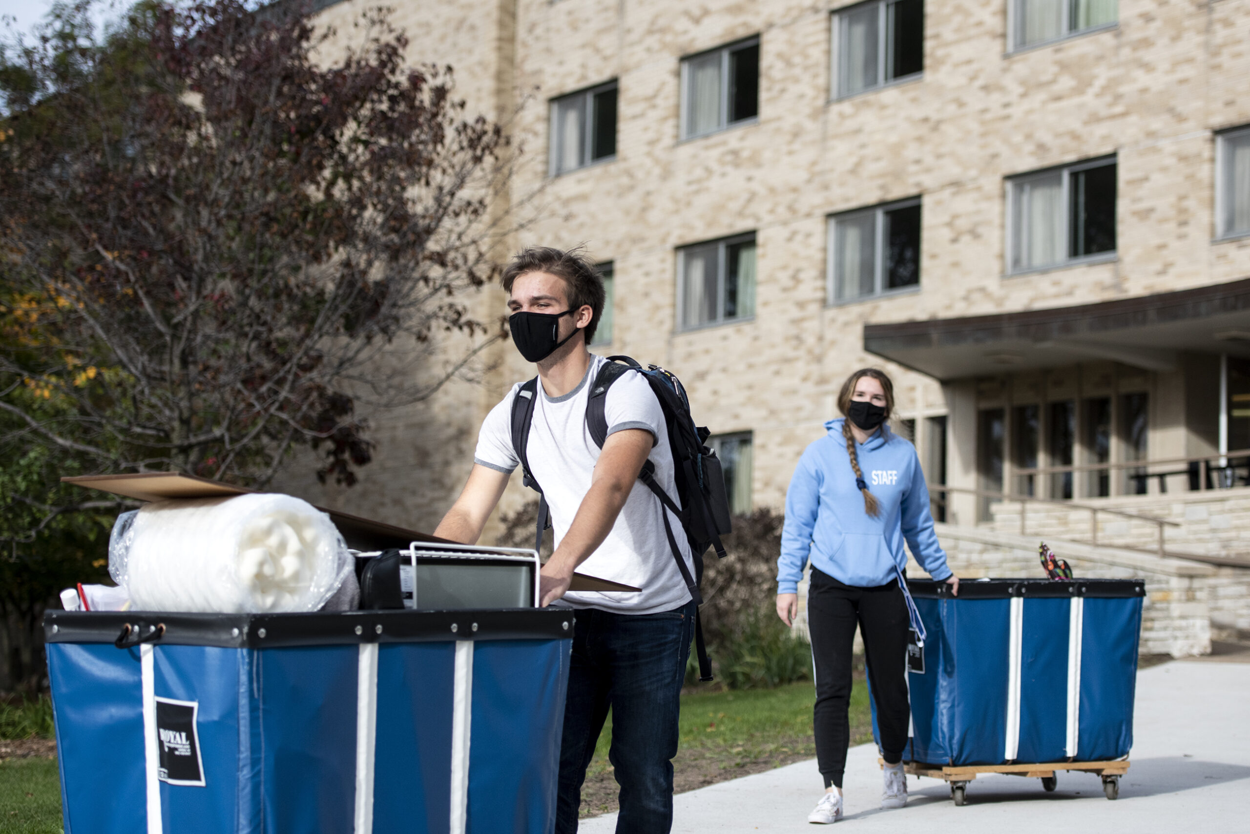 A student in a face mask rolls a blue bin filled with belongings