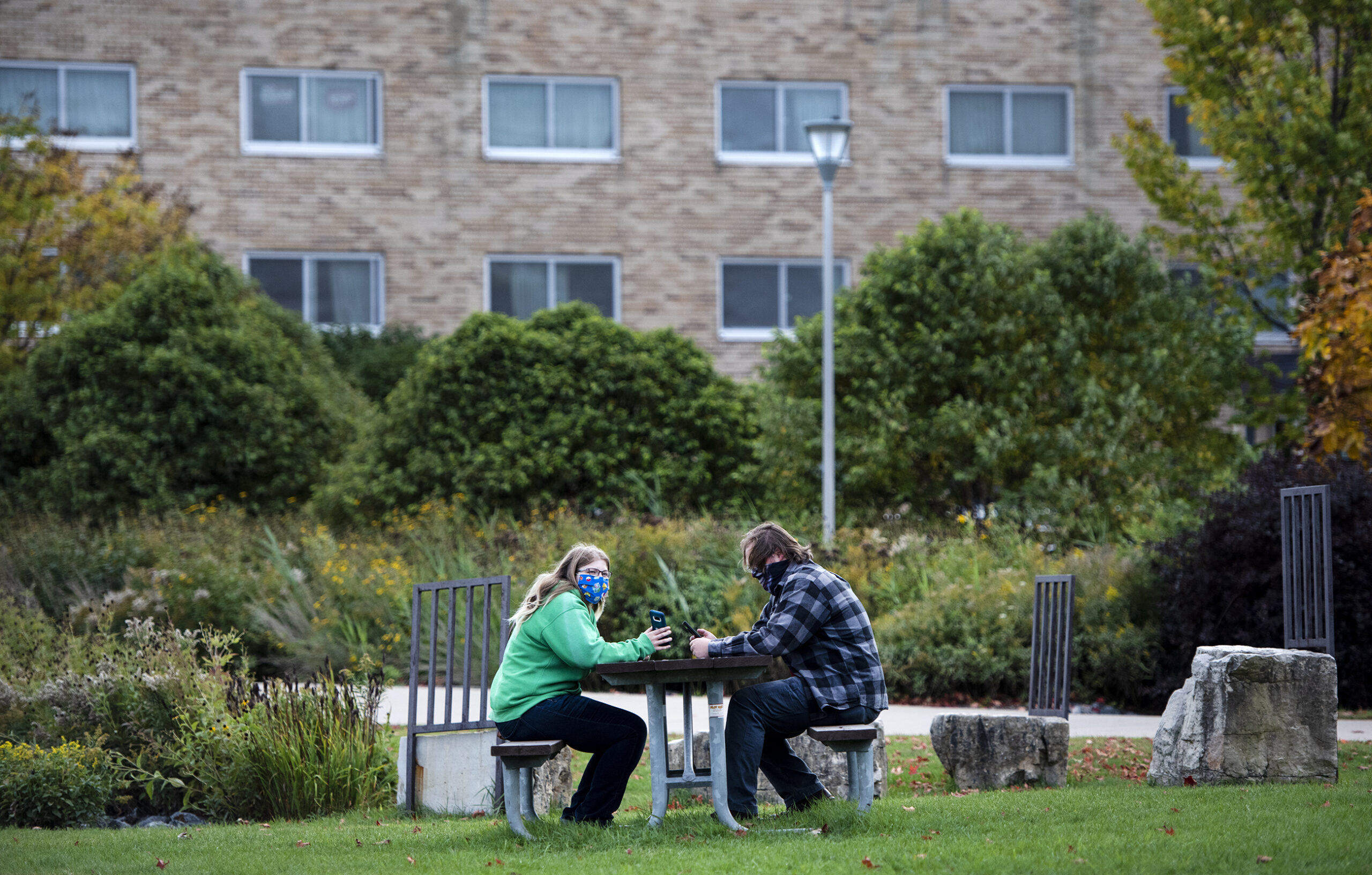 two people sit at a picnic table outdoors. a residence hall can be seen in the background.