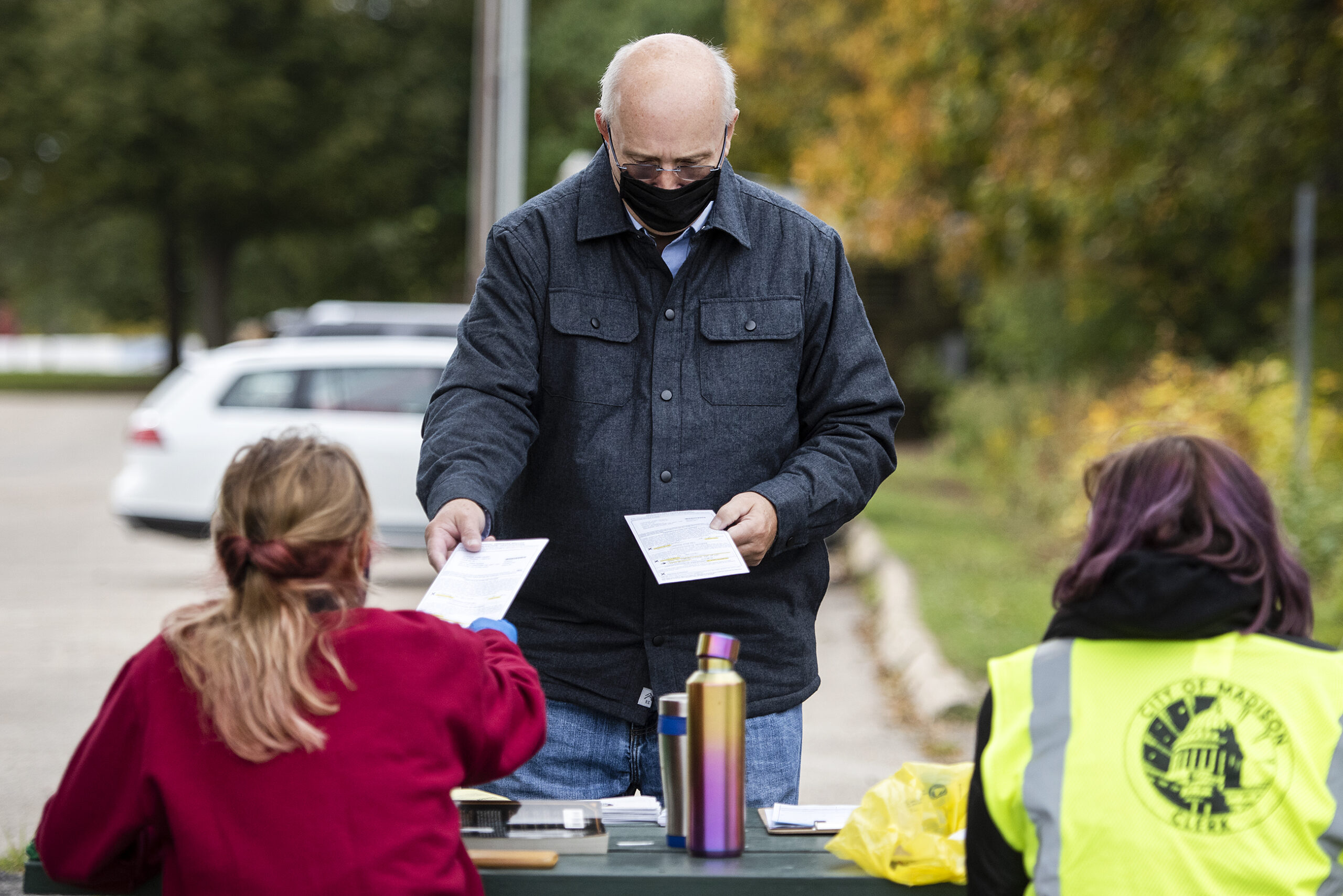 A man hands ballots to workers at a park table